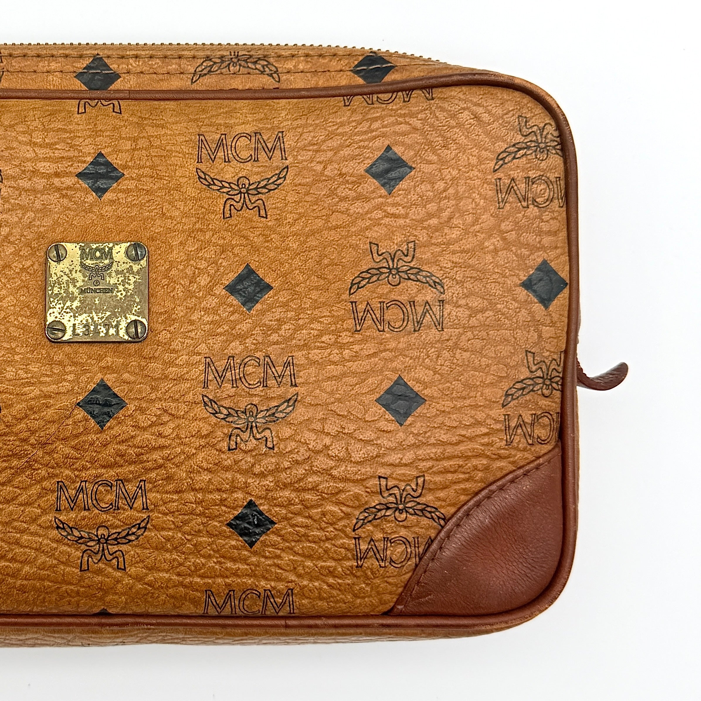 MCM Visetos monogram clutch bag in brown coated canvas with wristlet strap and gold logo plaque, photographed on white background.