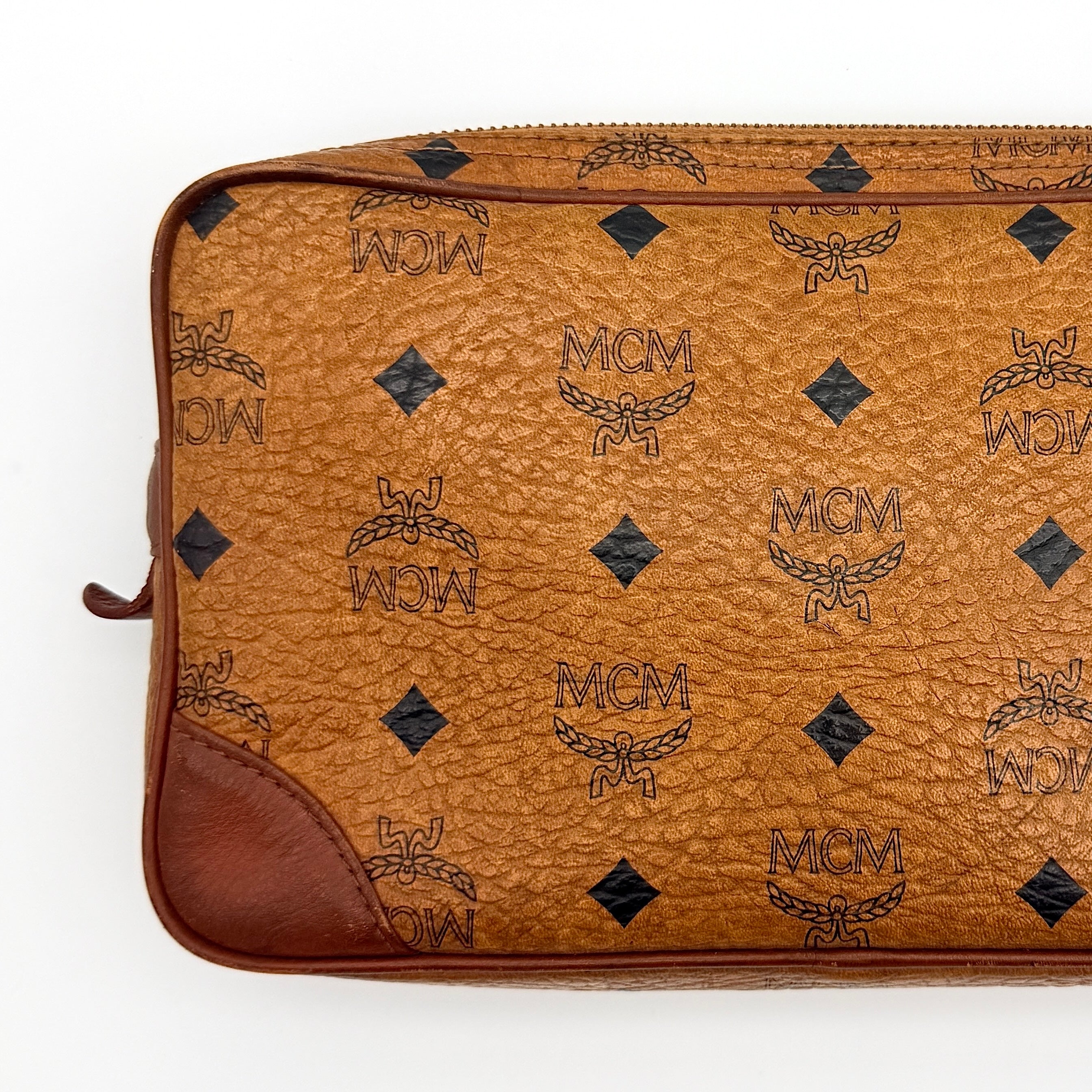 MCM Visetos monogram clutch bag in brown coated canvas with wristlet strap and gold logo plaque, photographed on white background.