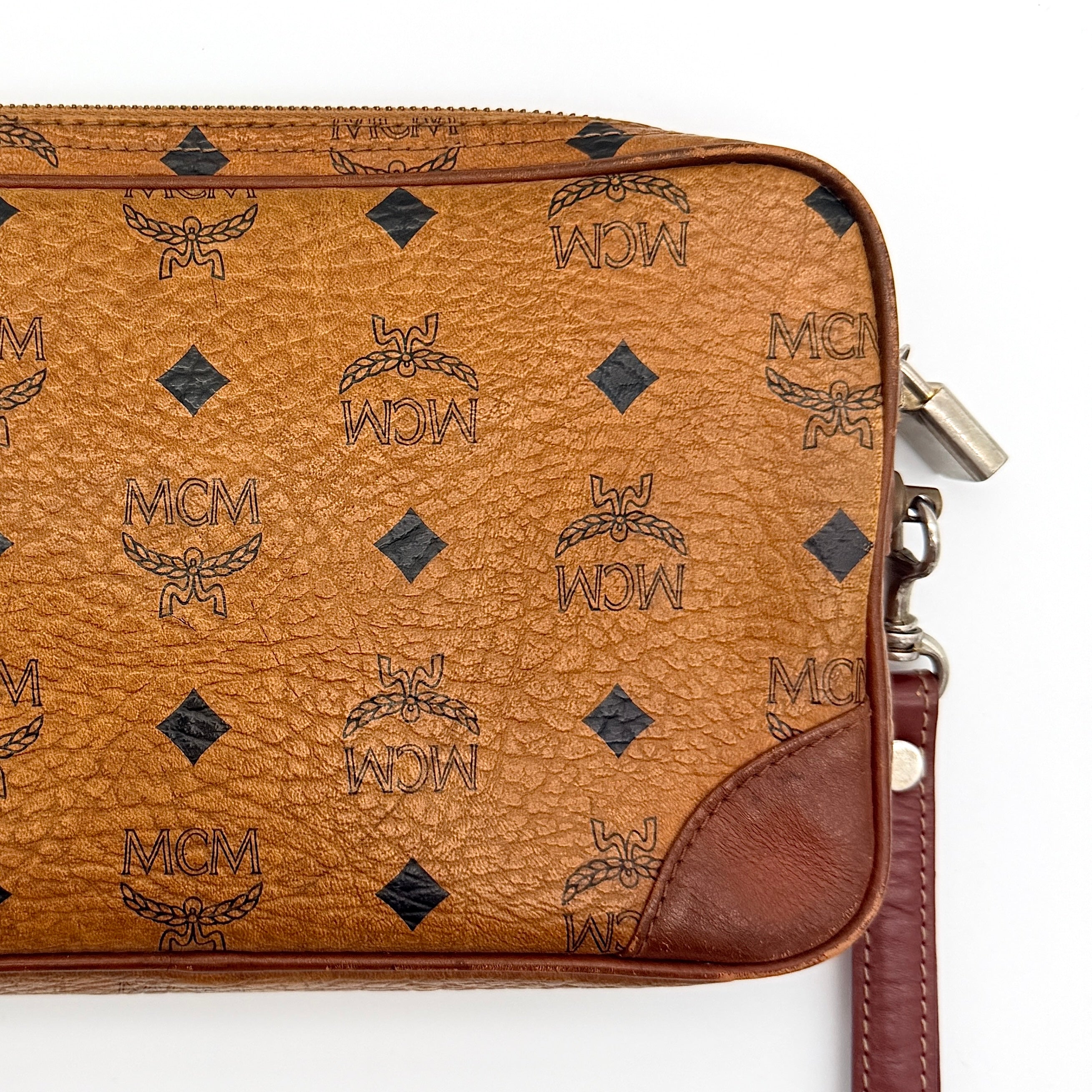 MCM Visetos monogram clutch bag in brown coated canvas with wristlet strap and gold logo plaque, photographed on white background.