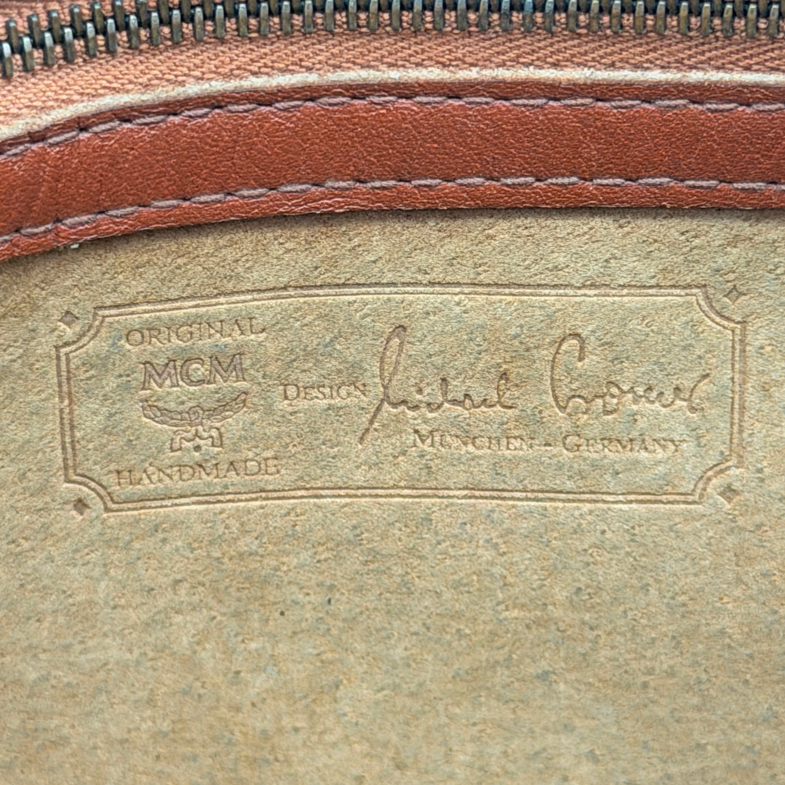 MCM Visetos monogram clutch bag in brown coated canvas with wristlet strap and gold logo plaque, photographed on white background.