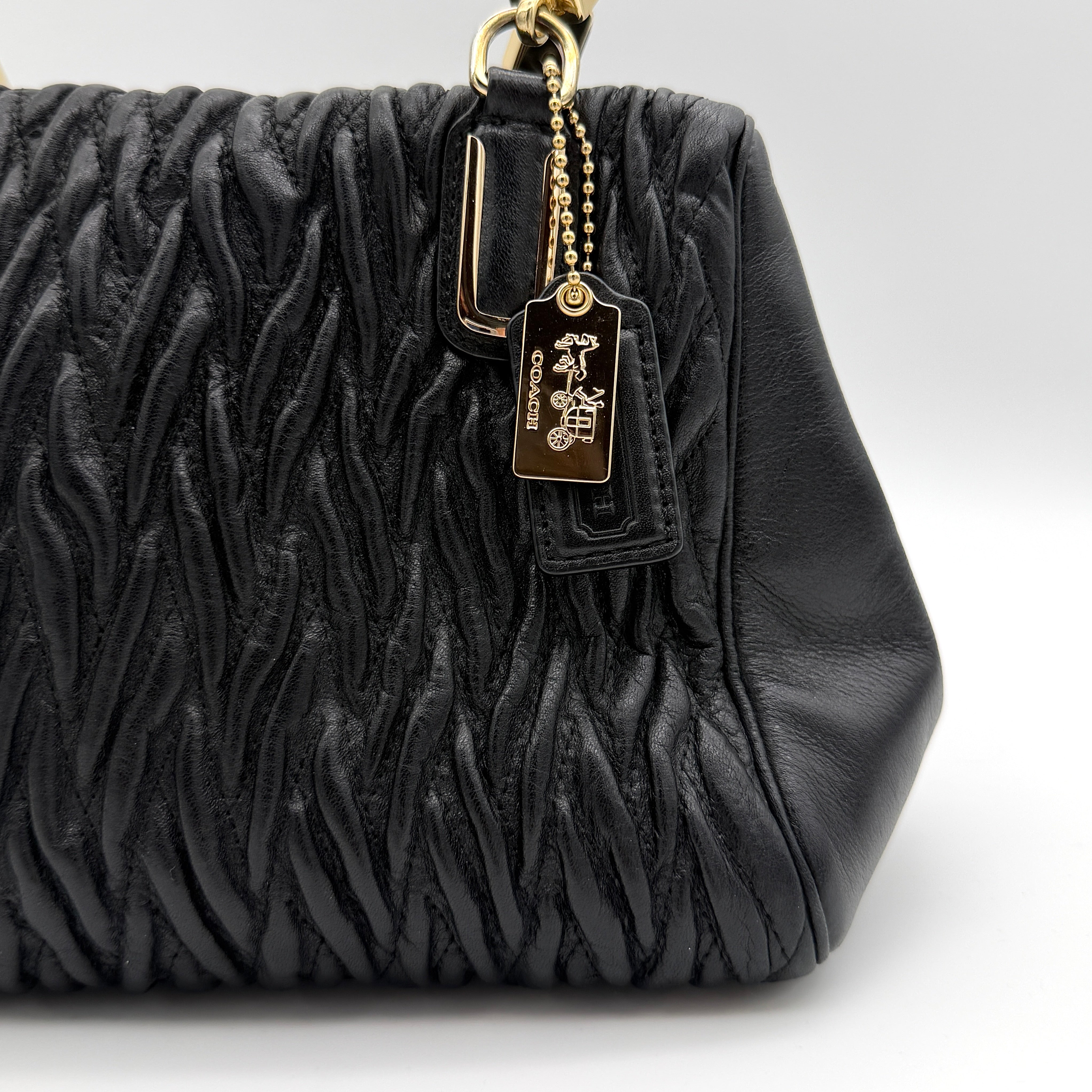 Coach Madison Gathered Twist satchel in black leather with gold hardware and detachable strap, styled on a white background.