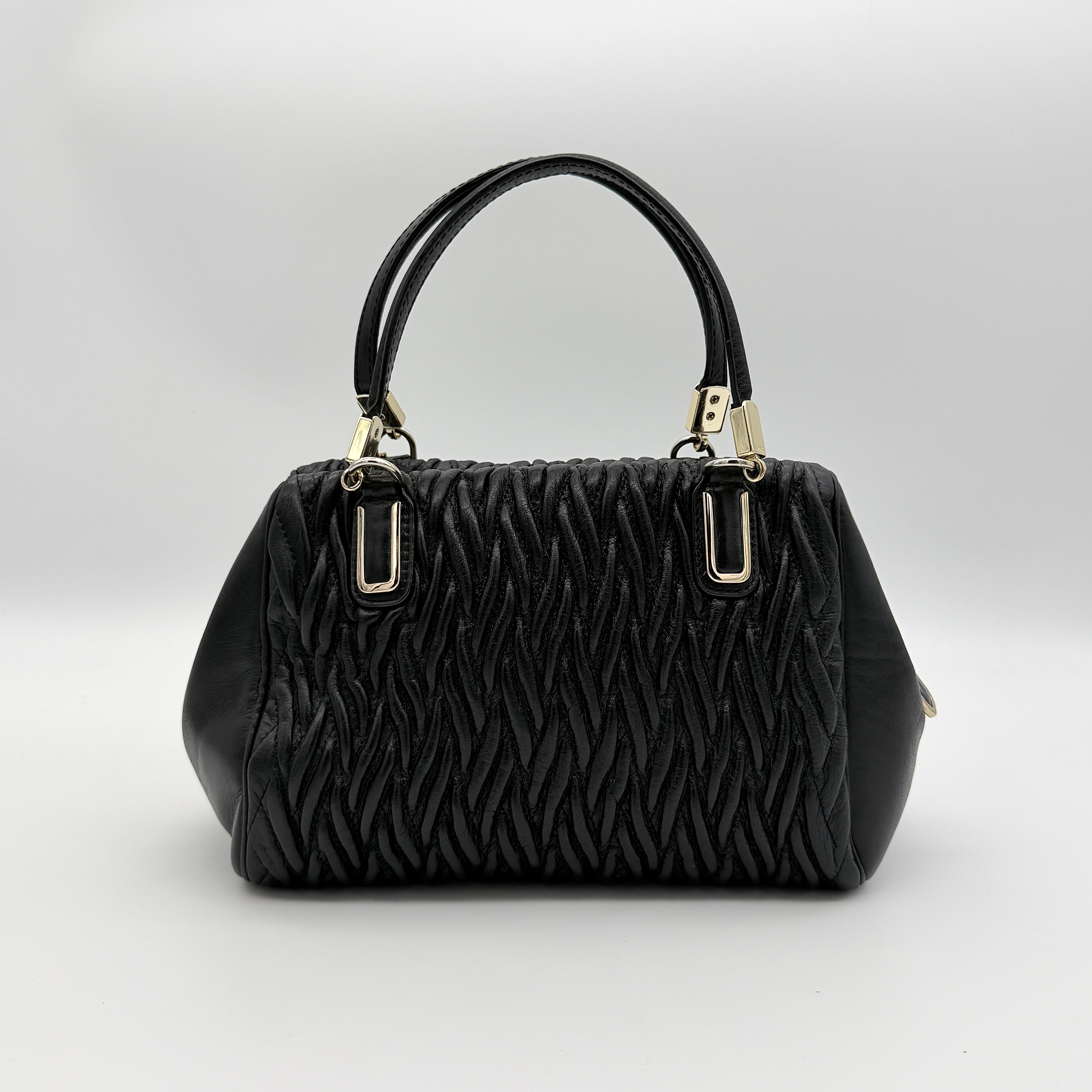 Coach Madison Gathered Twist satchel in black leather with gold hardware and detachable strap, styled on a white background.