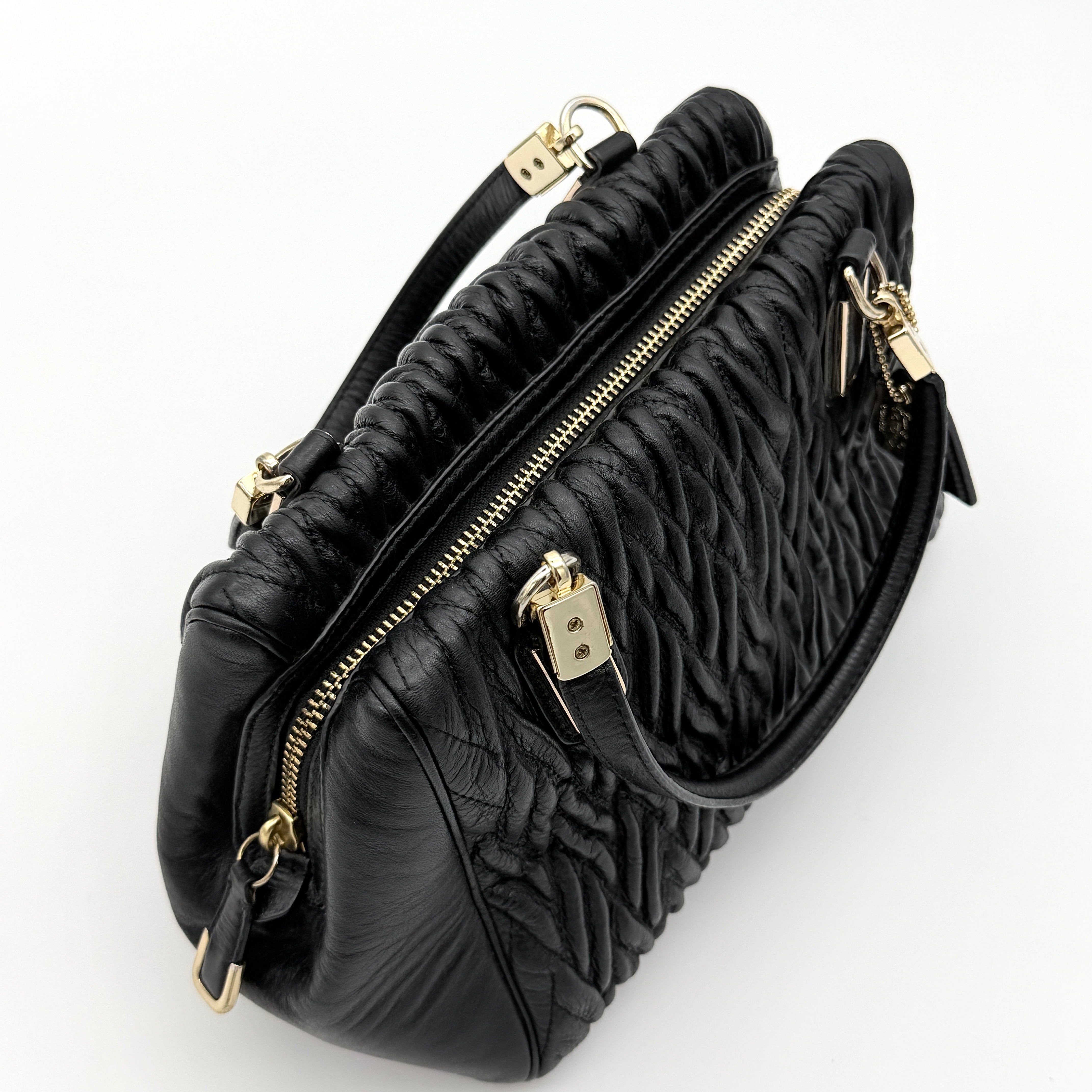 Coach Madison Gathered Twist satchel in black leather with gold hardware and detachable strap, styled on a white background.