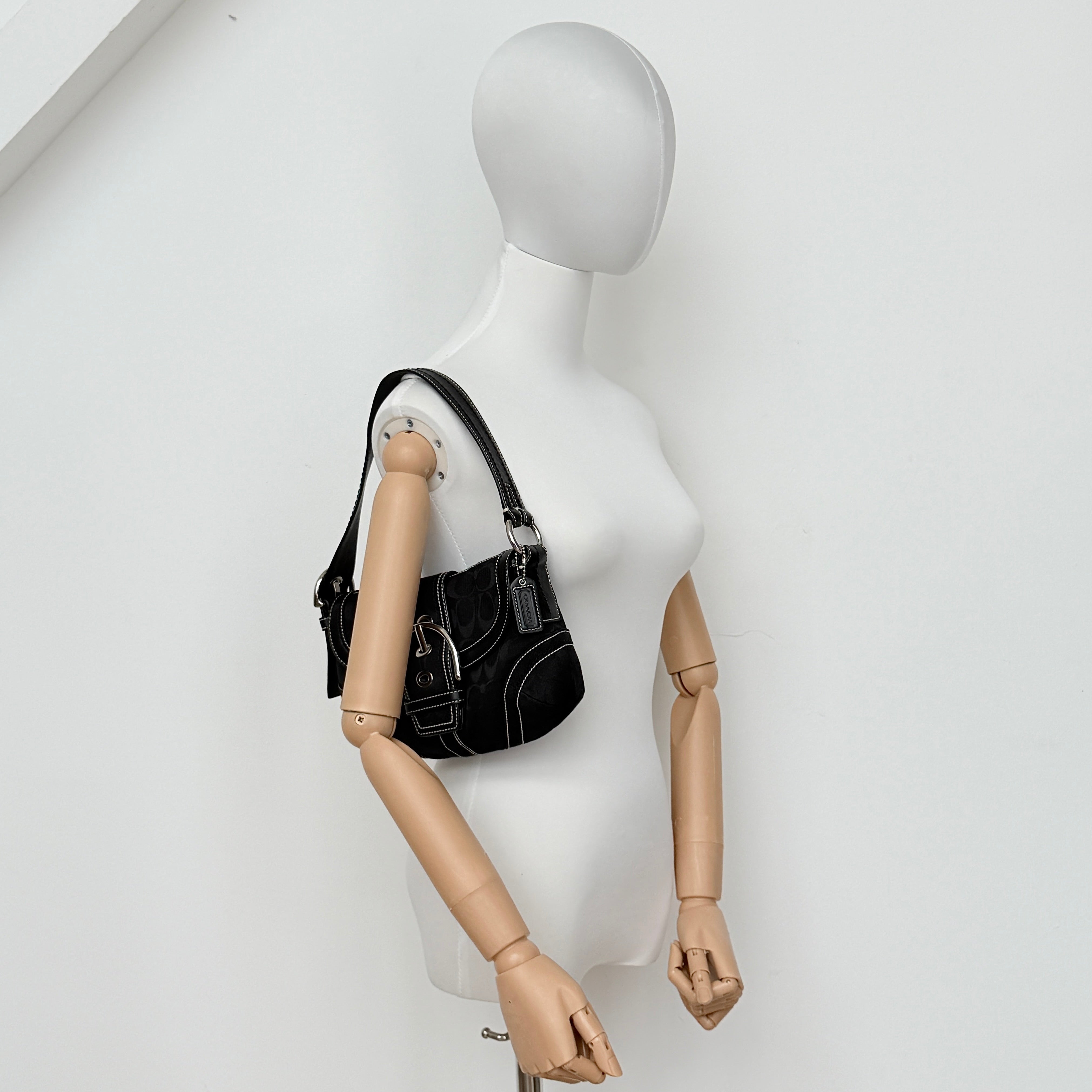 Coach black Signature Soho shoulder bag with oversized silver buckle, cream contrast stitching, and monogram jacquard canvas backdrop.