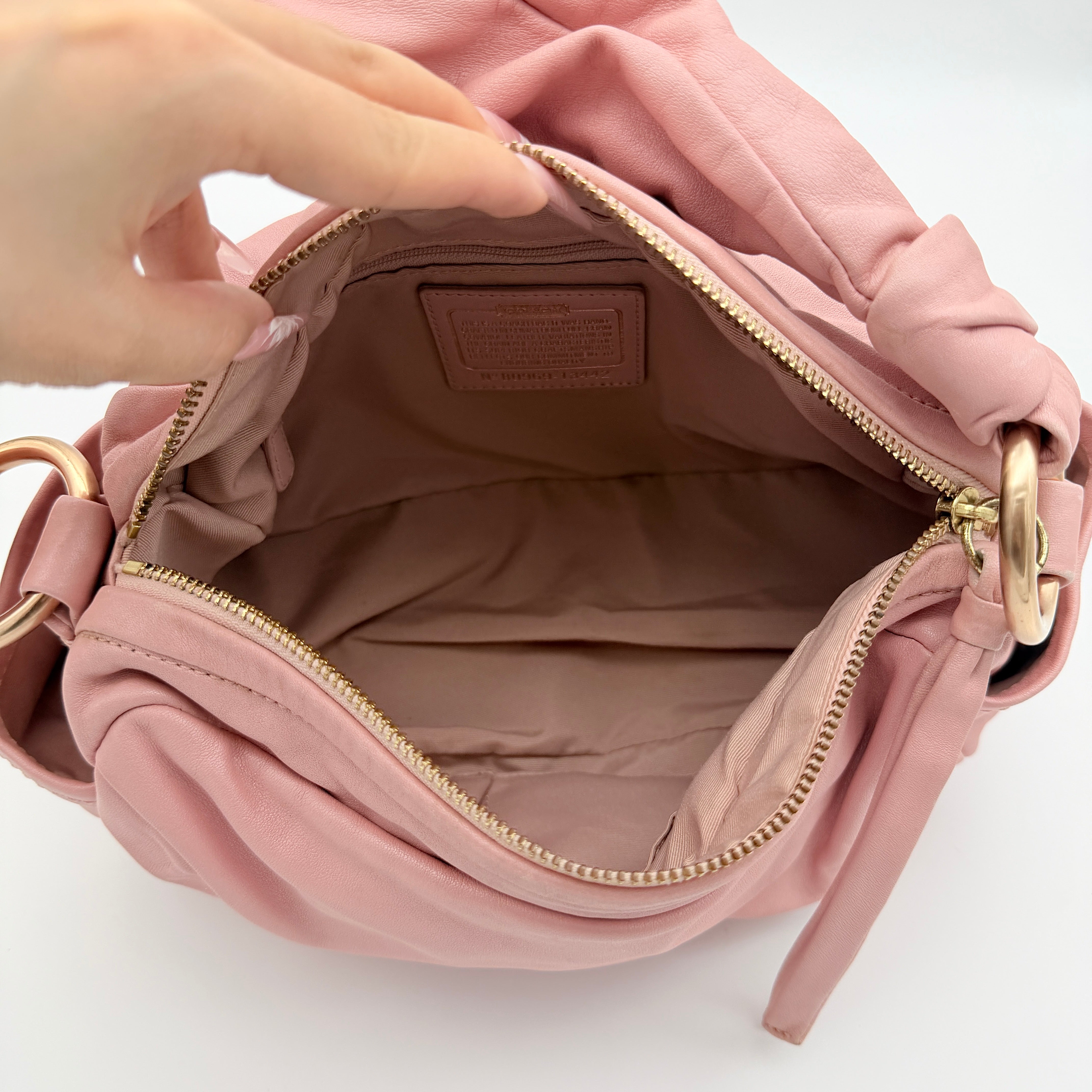 Coach pink leather hobo shoulder bag with knotted handle, gold-tone hardware, and side pockets.