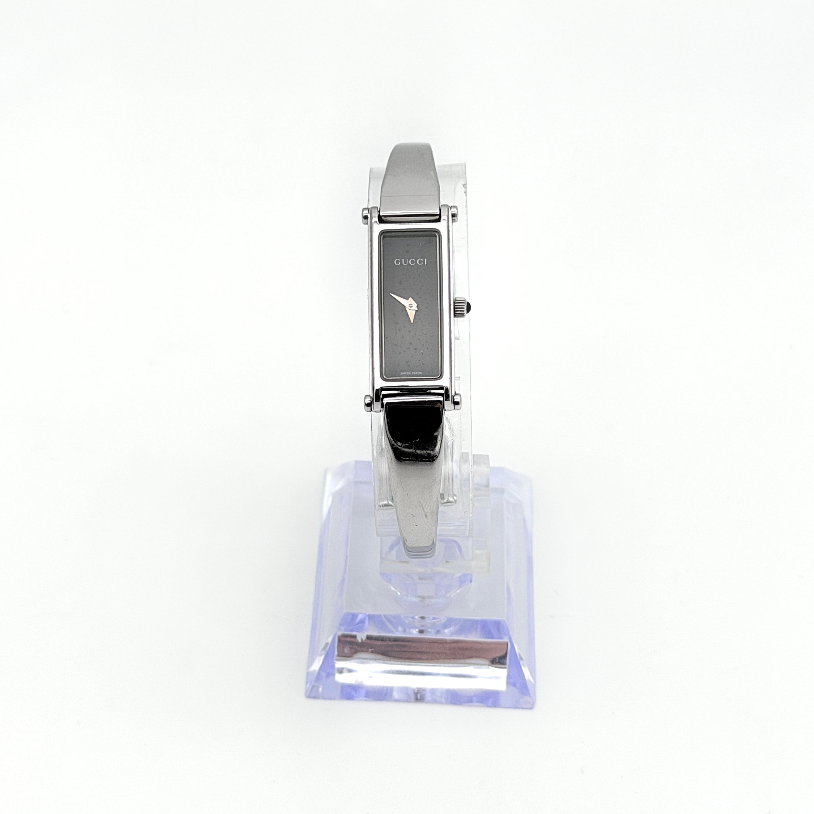 Gucci 1500L black dial bangle watch with stainless steel bracelet, photographed on a clear display stand.
