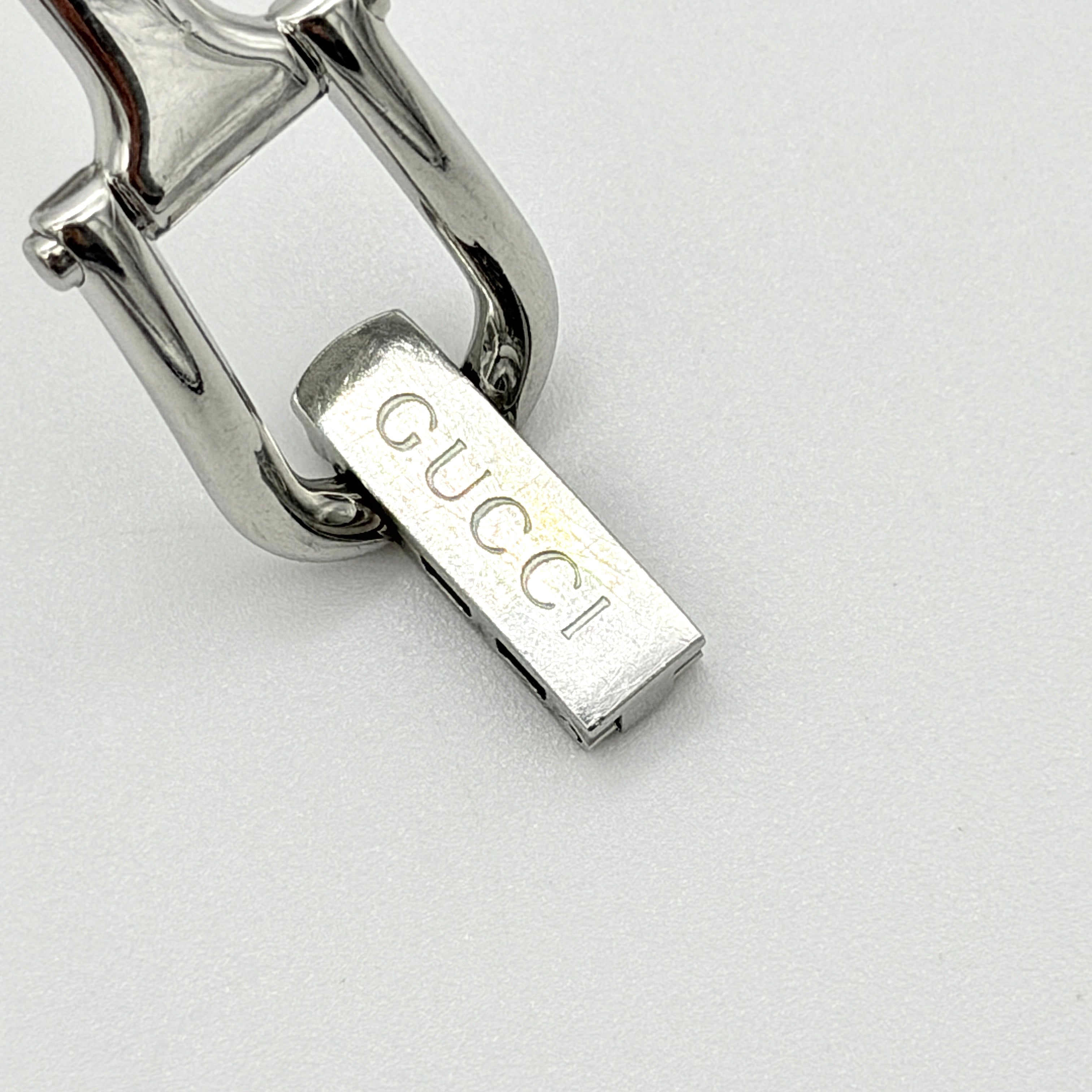 Gucci 1500L black dial bangle watch with stainless steel bracelet, photographed on a clear display stand.