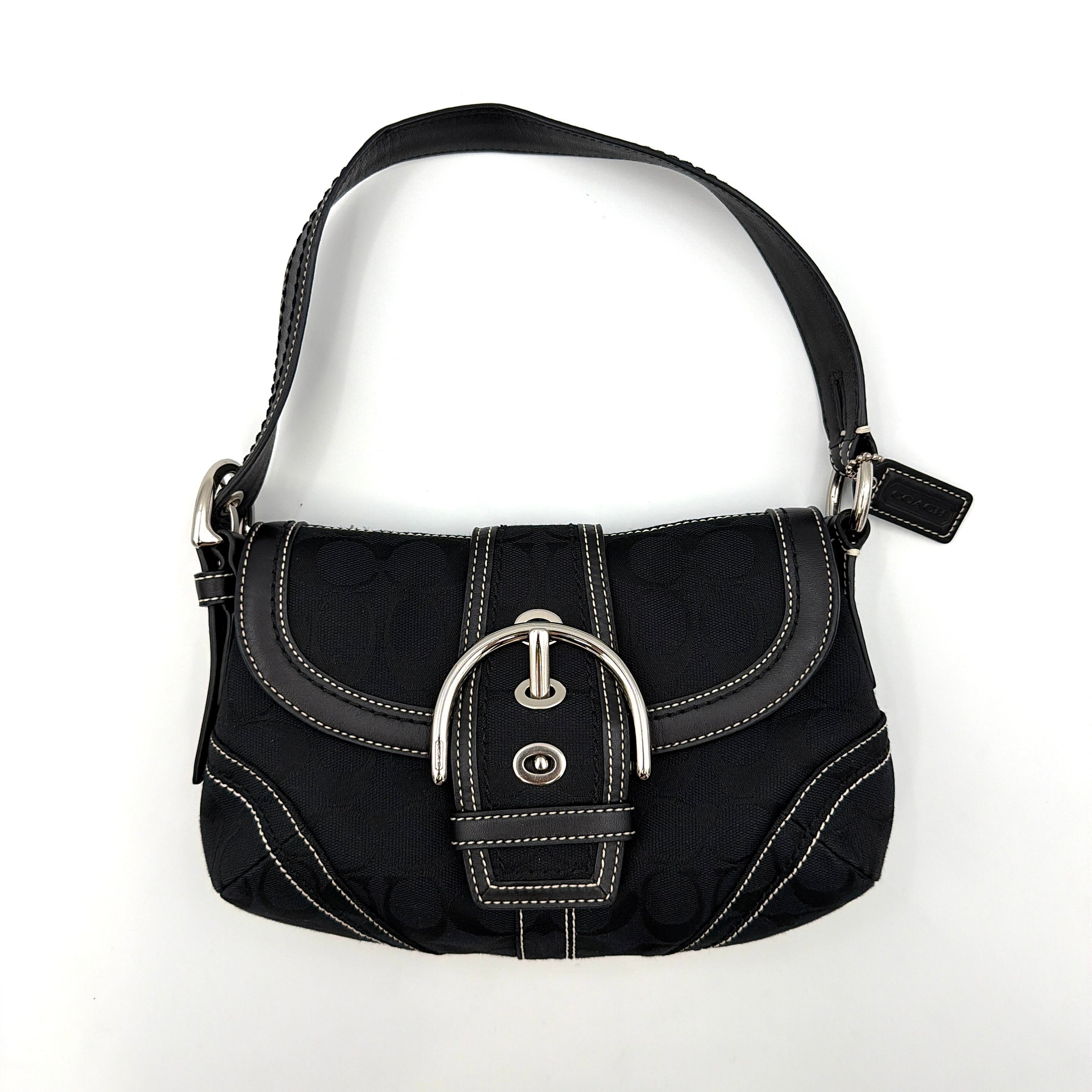 Coach black Signature Soho shoulder bag with oversized silver buckle, cream contrast stitching, and monogram jacquard canvas backdrop.