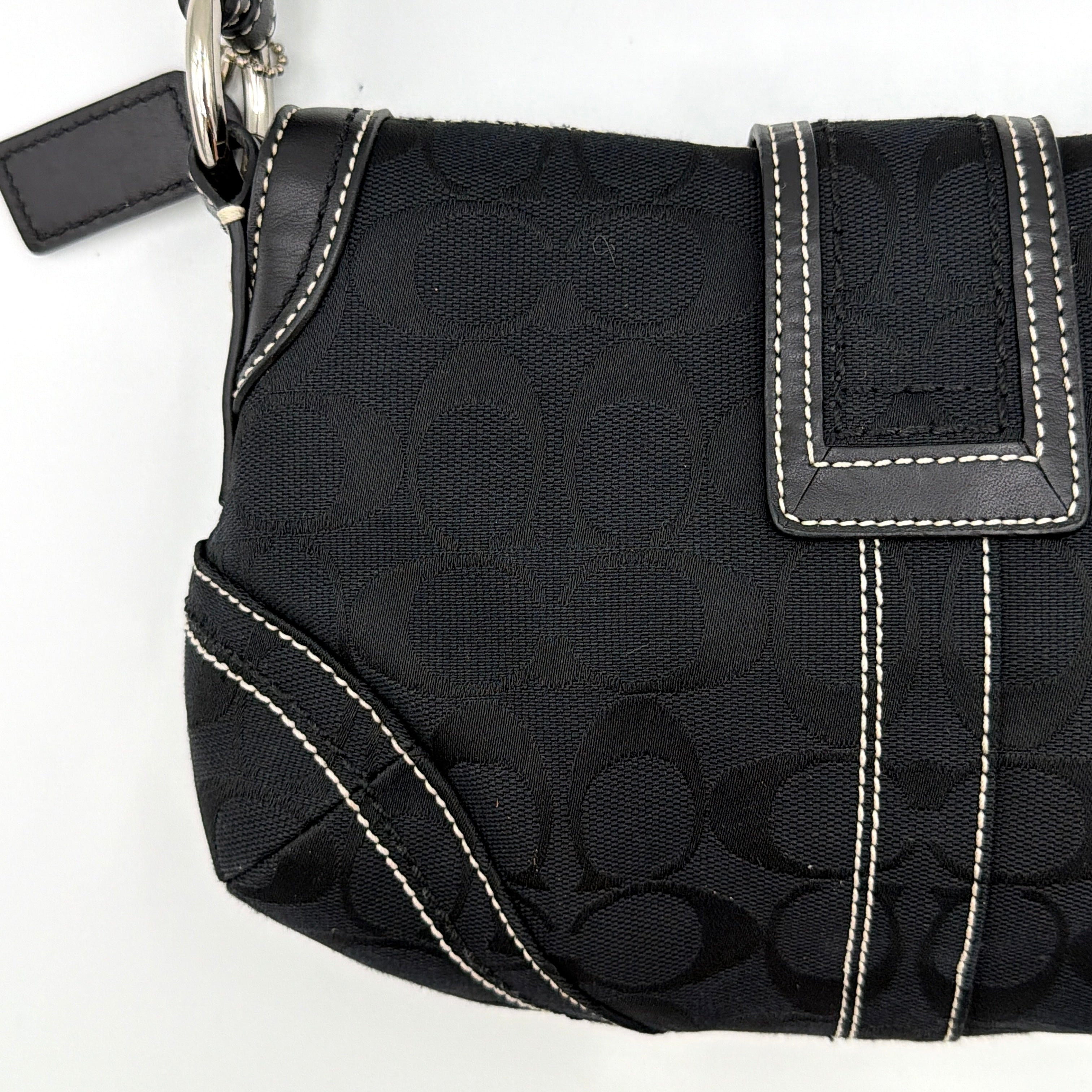 Coach black Signature Soho shoulder bag with oversized silver buckle, cream contrast stitching, and monogram jacquard canvas backdrop.