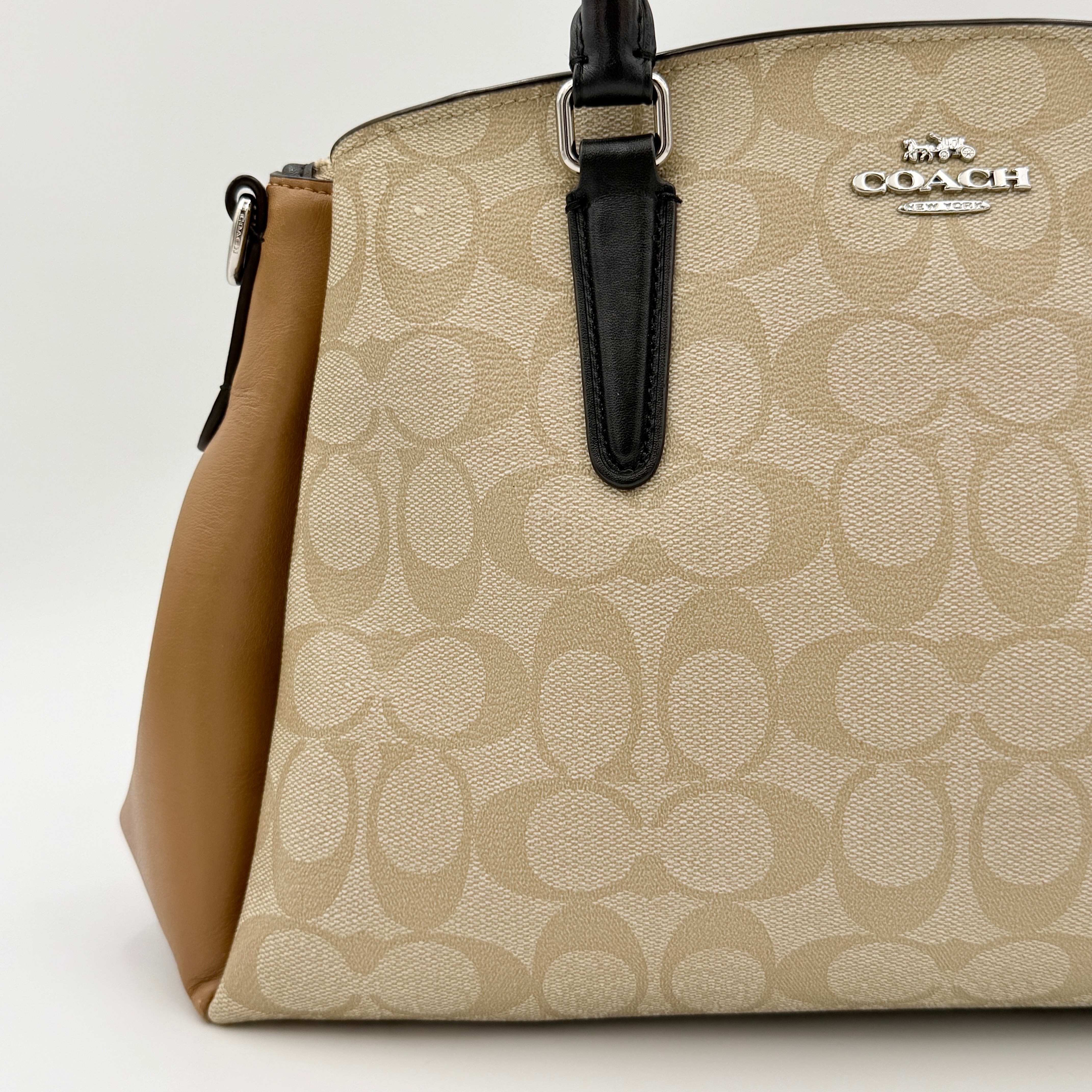 Coach Signature Sage Carryall in beige monogram canvas and tan leather with black handles, styled as an elegant, softly structured handbag.