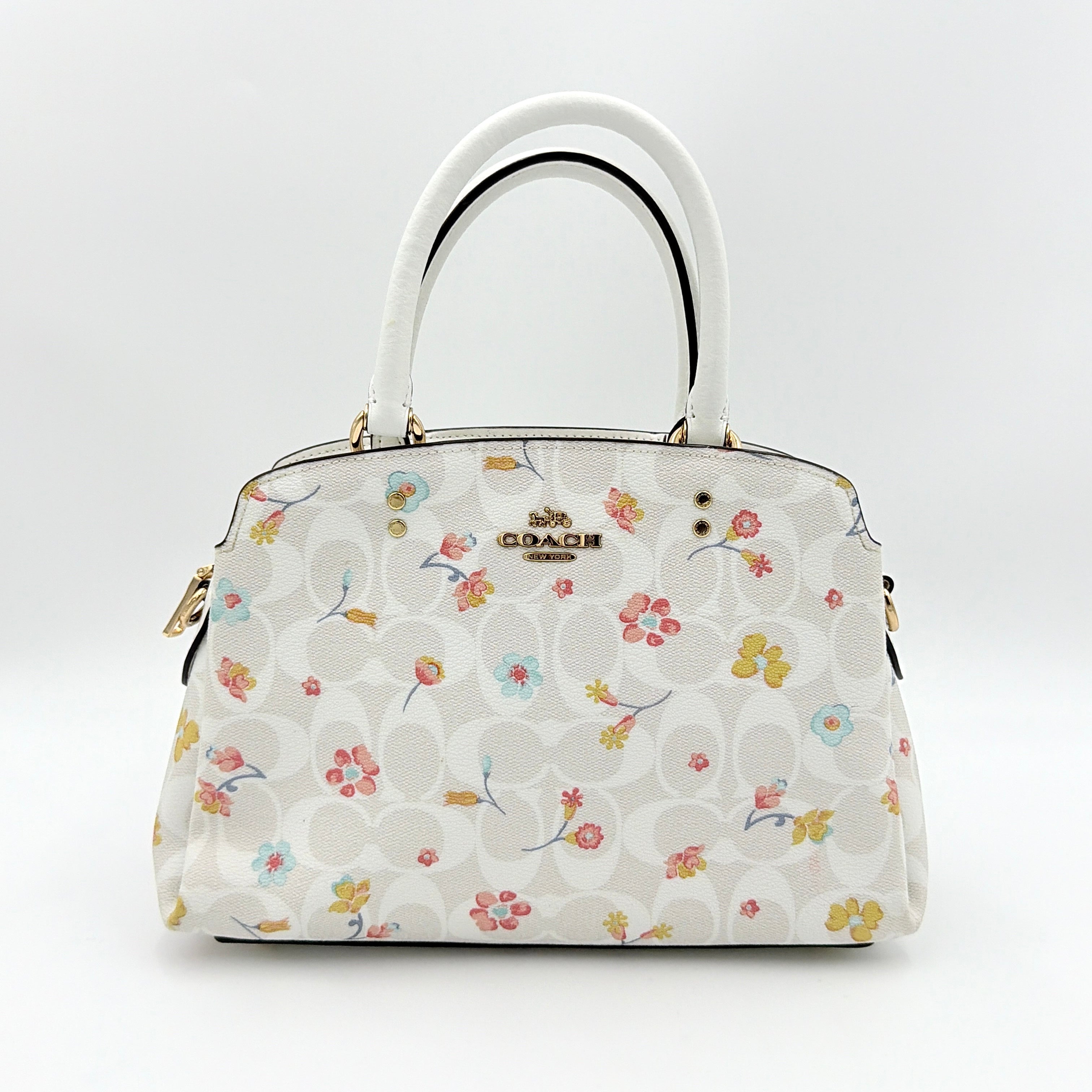 Coach 2Way Signature Lillie Carryall in white canvas with gold hardware and multicolour floral print, accompanied by a detachable white shoulder strap.