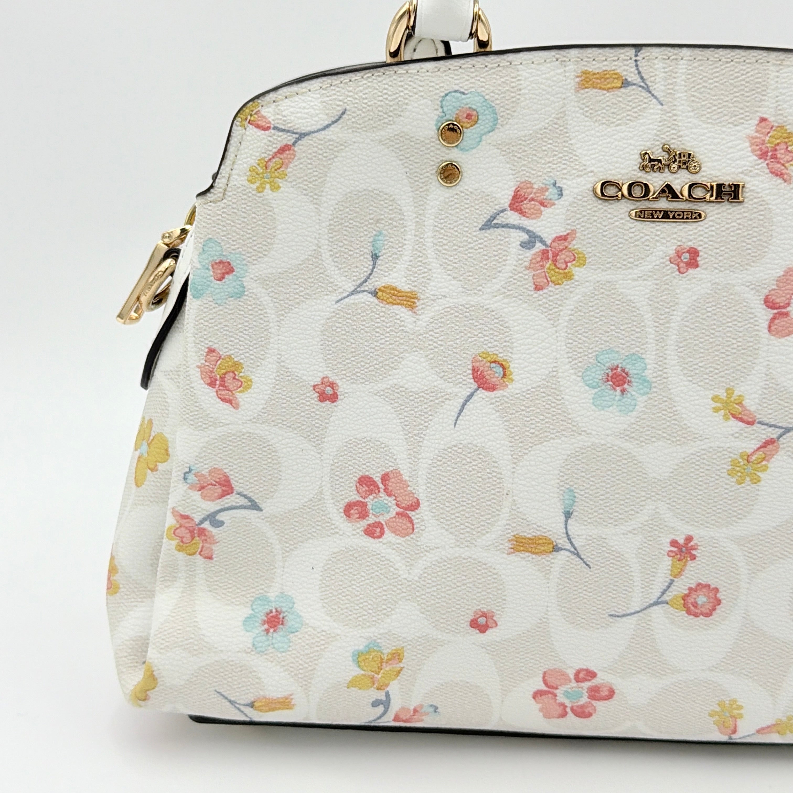 Coach 2Way Signature Lillie Carryall in white canvas with gold hardware and multicolour floral print, accompanied by a detachable white shoulder strap.