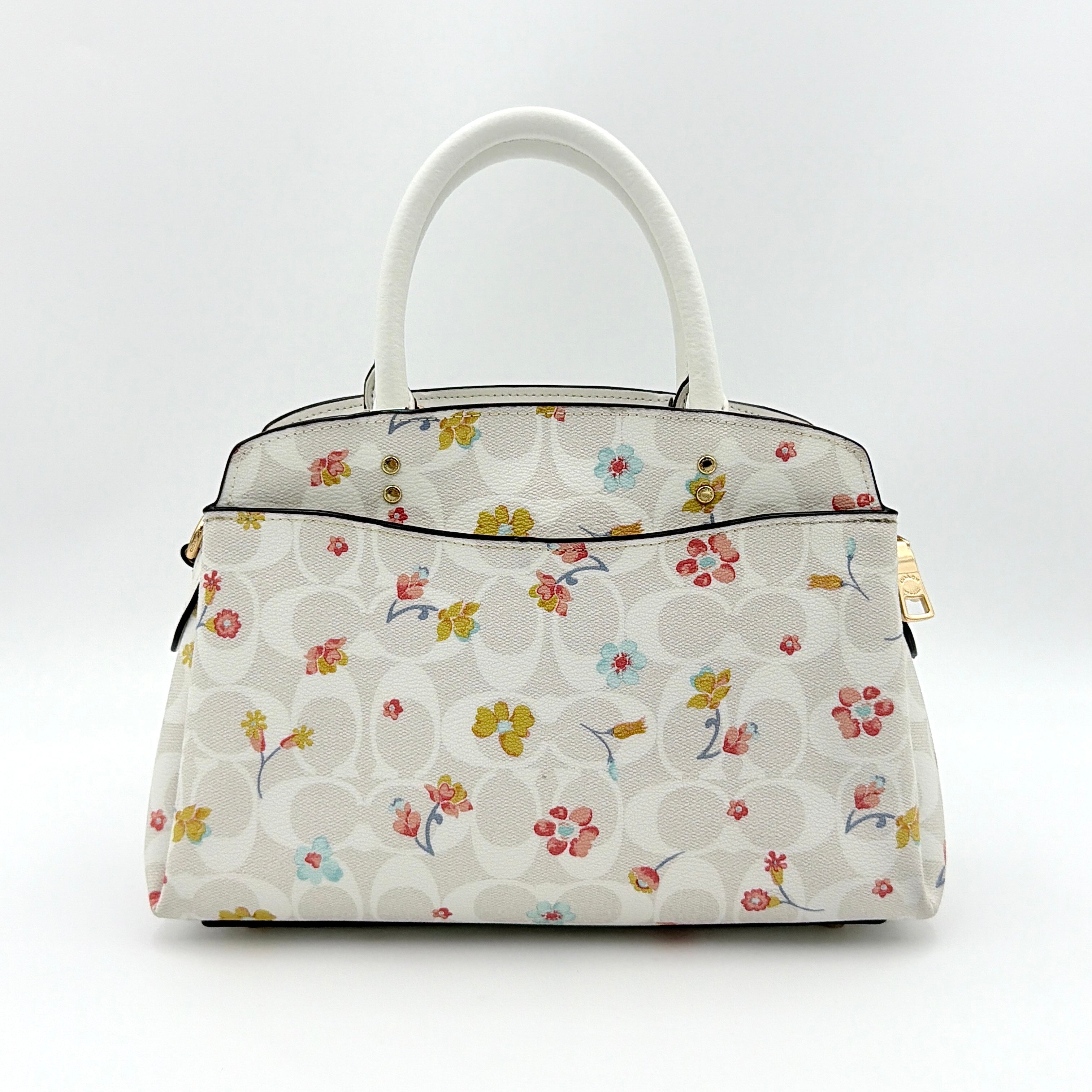 Coach 2Way Signature Lillie Carryall in white canvas with gold hardware and multicolour floral print, accompanied by a detachable white shoulder strap.