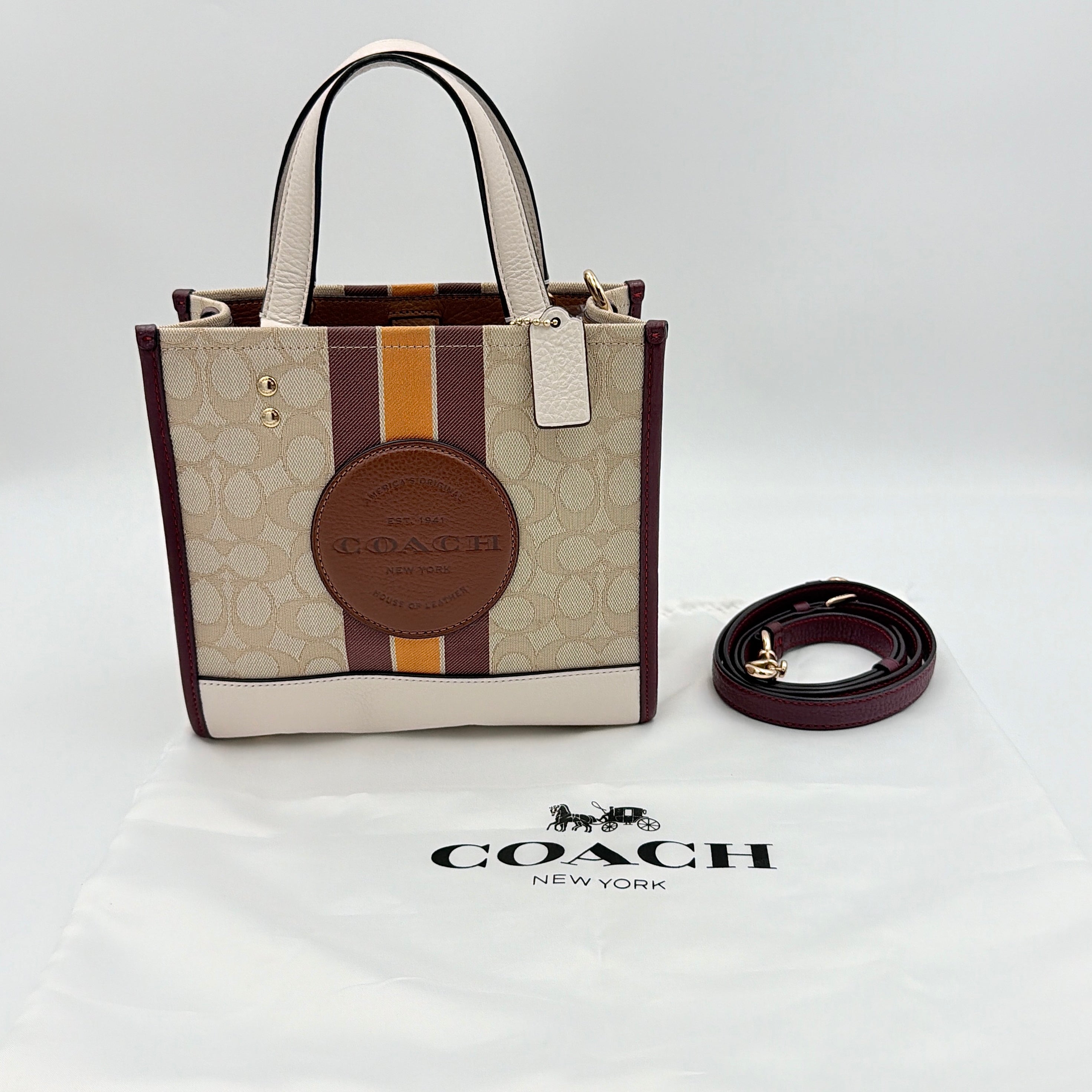 Coach Signature Dempsey 22 Stripe Tote Bag in beige canvas with bold vertical stripes, leather trims, logo patch, and detachable strap.