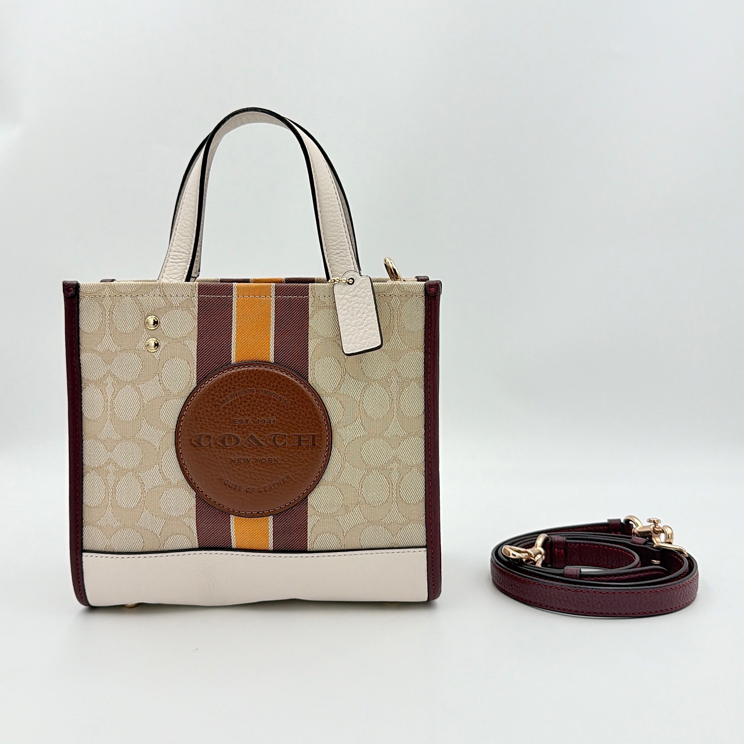 Coach Signature Dempsey 22 Stripe Tote Bag in beige canvas with bold vertical stripes, leather trims, logo patch, and detachable strap.