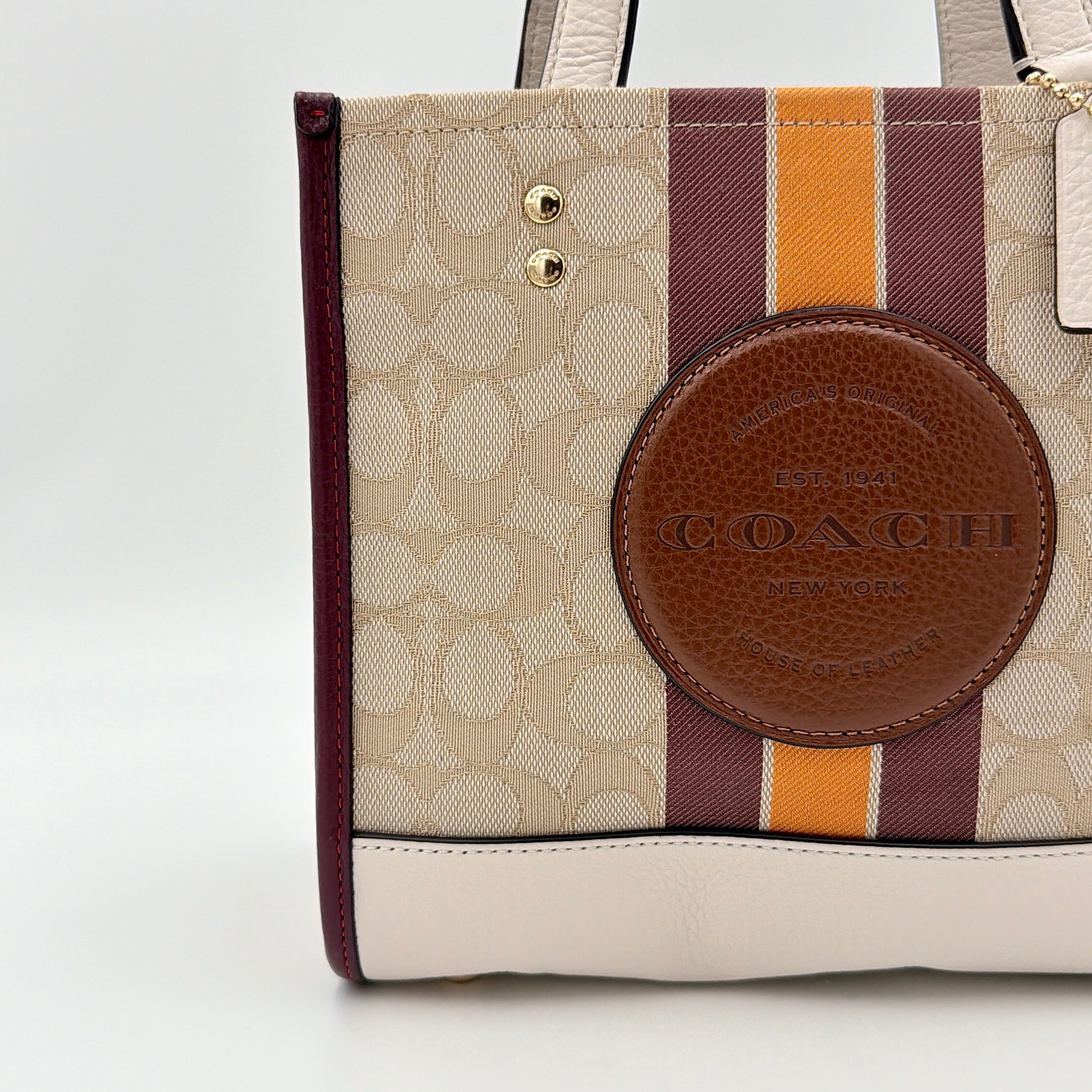 Coach Signature Dempsey 22 Stripe Tote Bag in beige canvas with bold vertical stripes, leather trims, logo patch, and detachable strap.