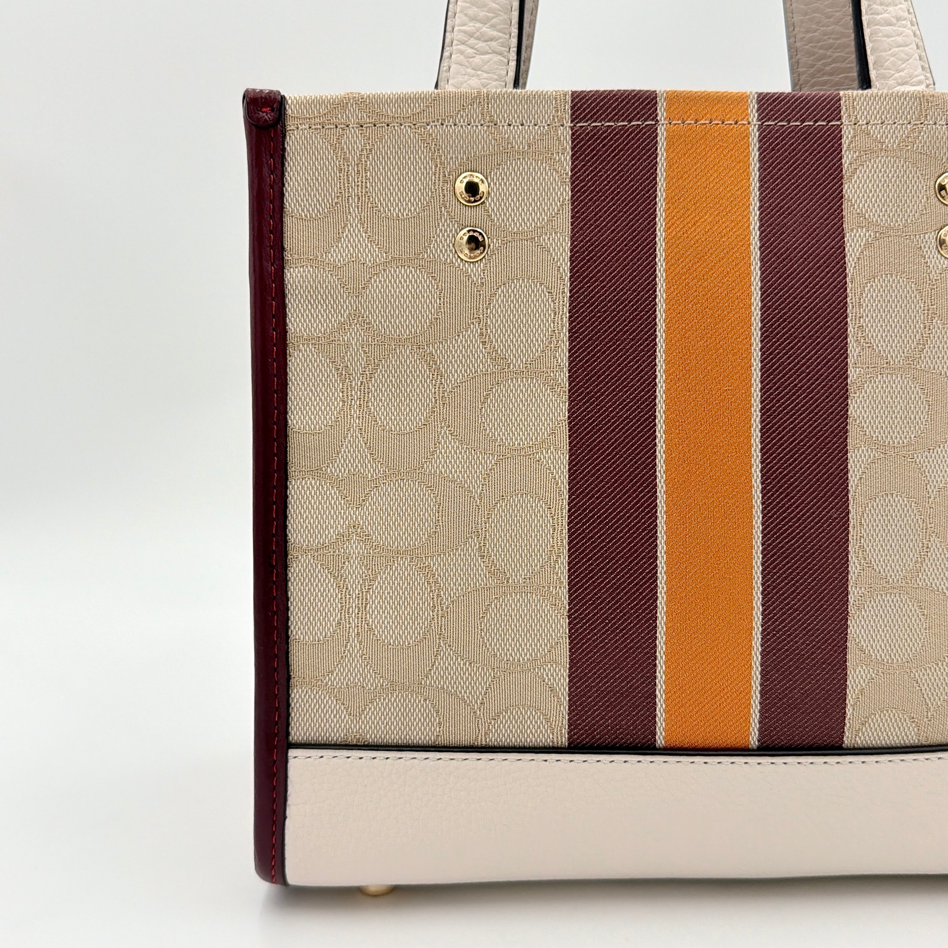 Coach Signature Dempsey 22 Stripe Tote Bag in beige canvas with bold vertical stripes, leather trims, logo patch, and detachable strap.