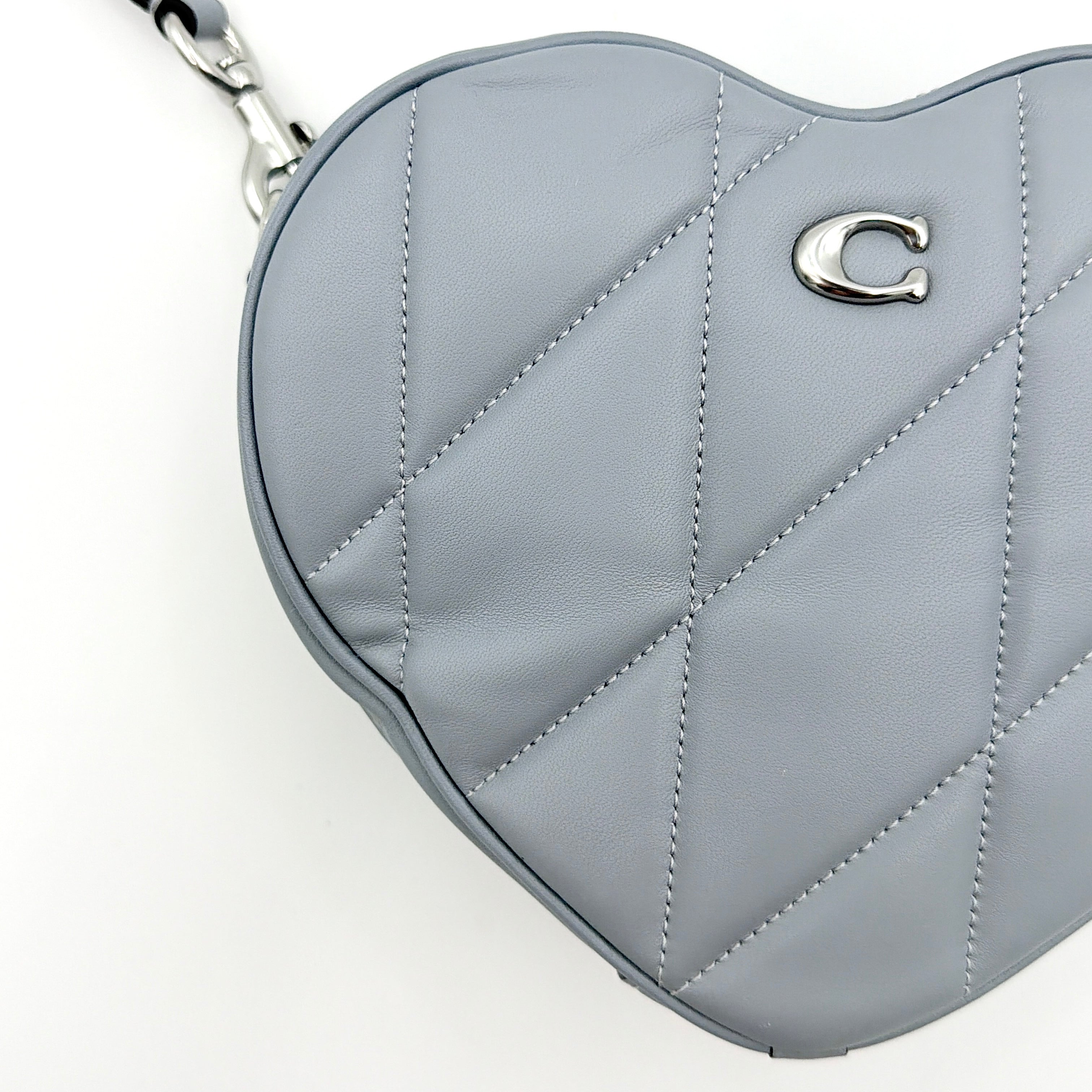Coach heart-shaped quilted grey crossbody bag with silver hardware and adjustable strap.