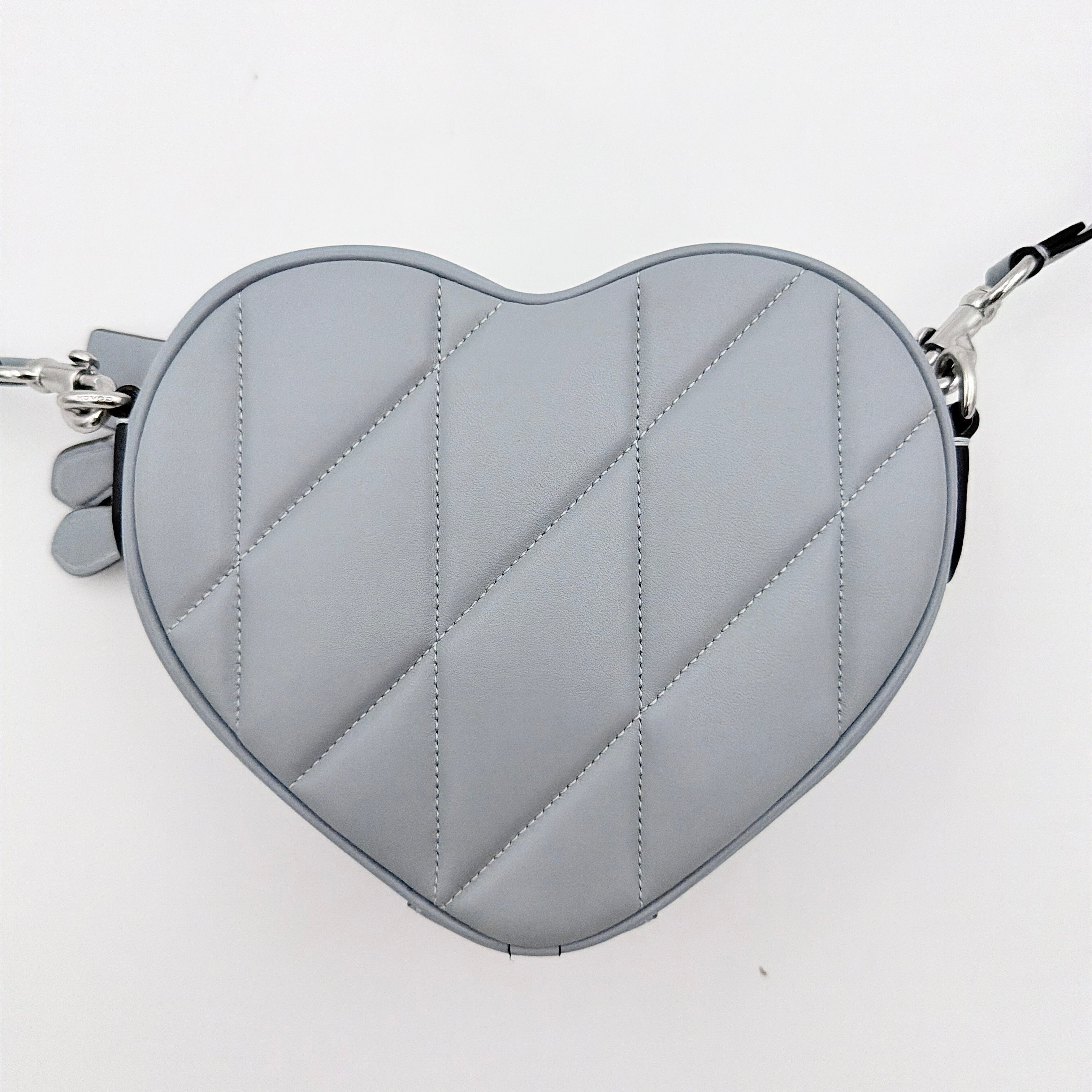 Coach heart-shaped quilted grey crossbody bag with silver hardware and adjustable strap.