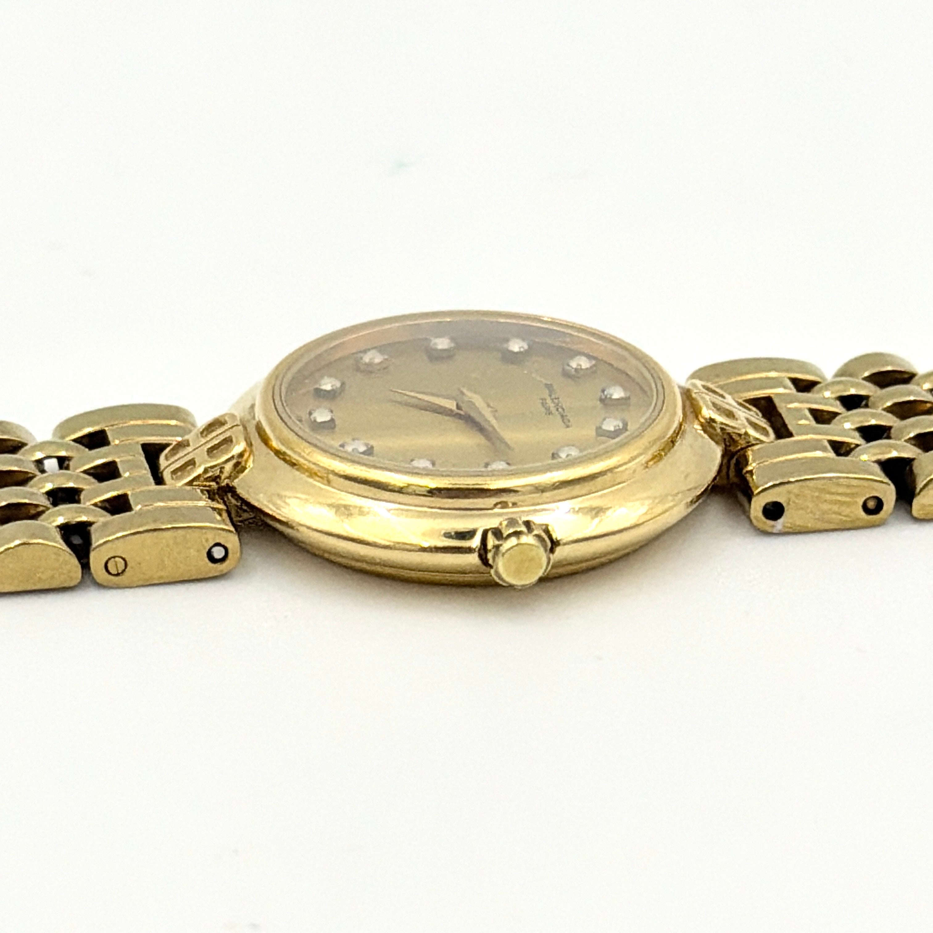 Balenciaga BB Quartz gold watch with a round dial, diamond-shaped hour markers, and a gold link bracelet displayed on a black cushion.