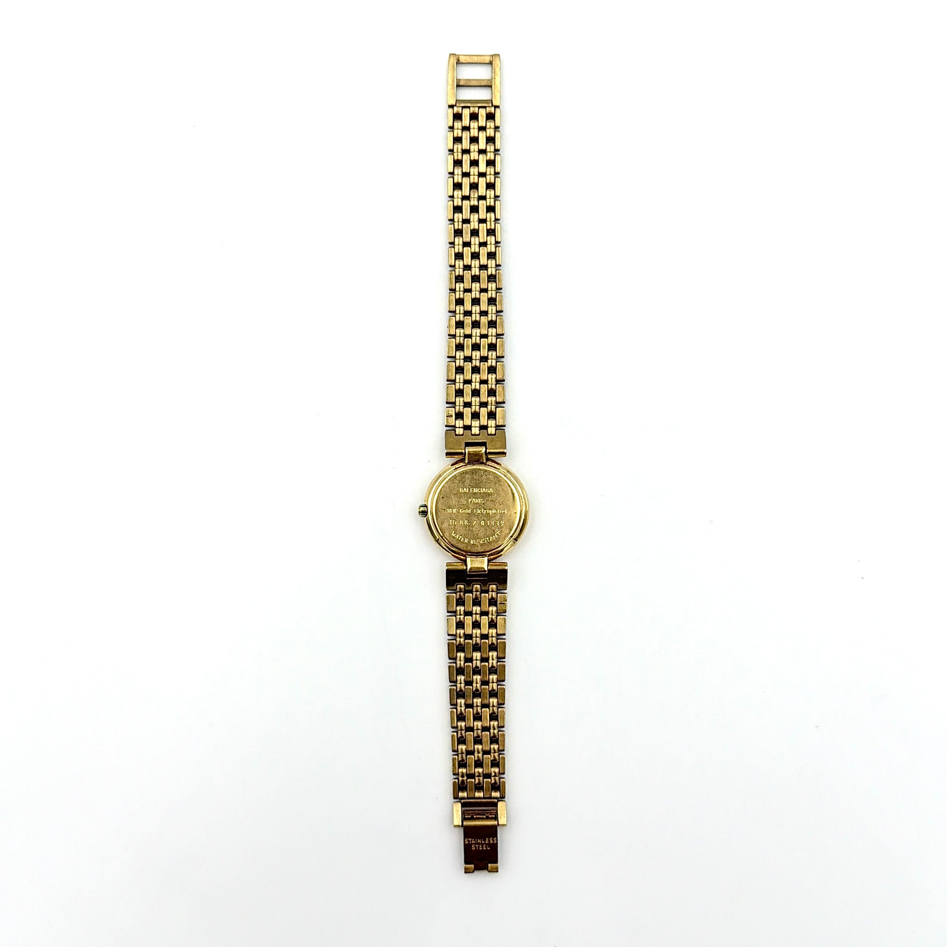 Balenciaga BB Quartz gold watch with a round dial, diamond-shaped hour markers, and a gold link bracelet displayed on a black cushion.