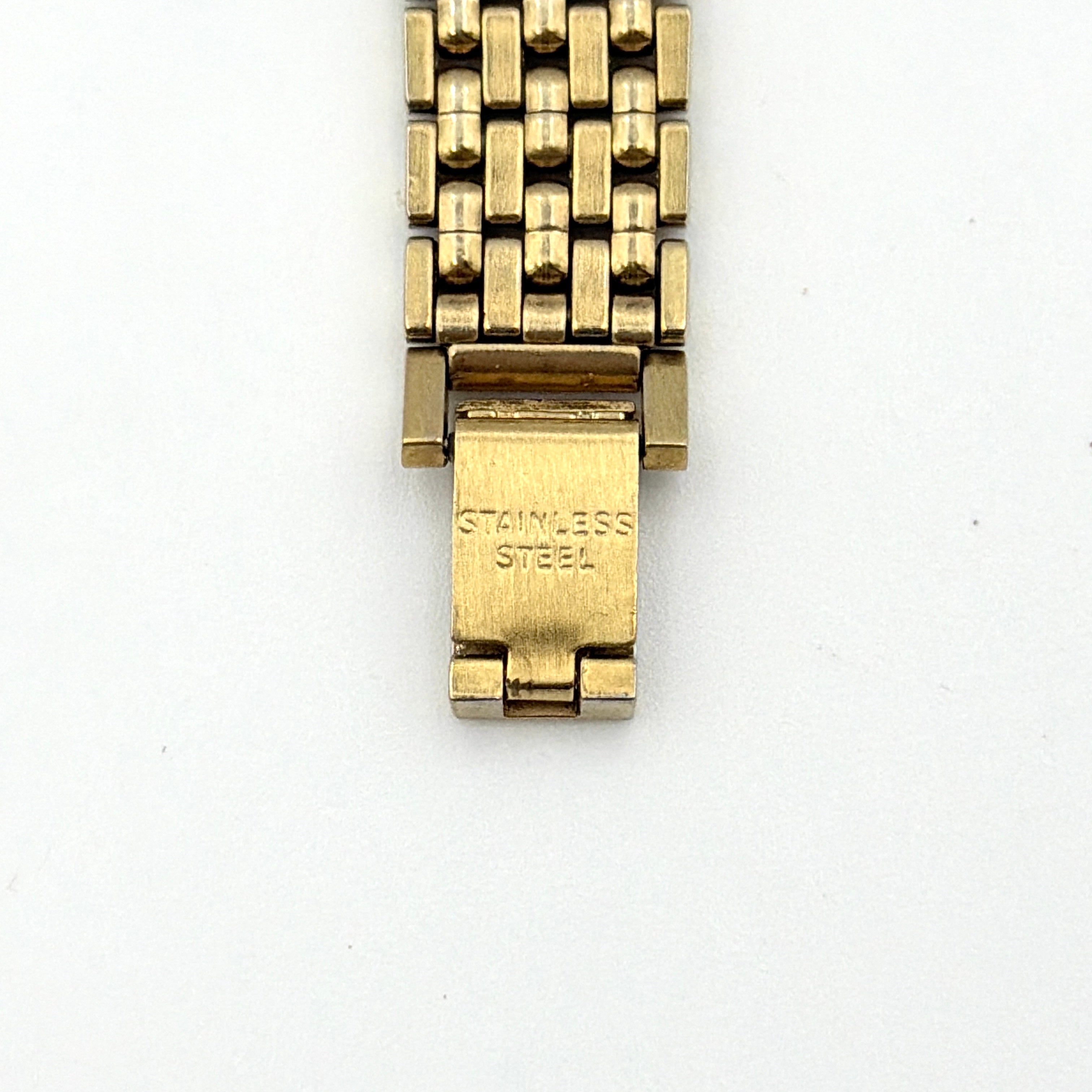 Balenciaga BB Quartz gold watch with a round dial, diamond-shaped hour markers, and a gold link bracelet displayed on a black cushion.
