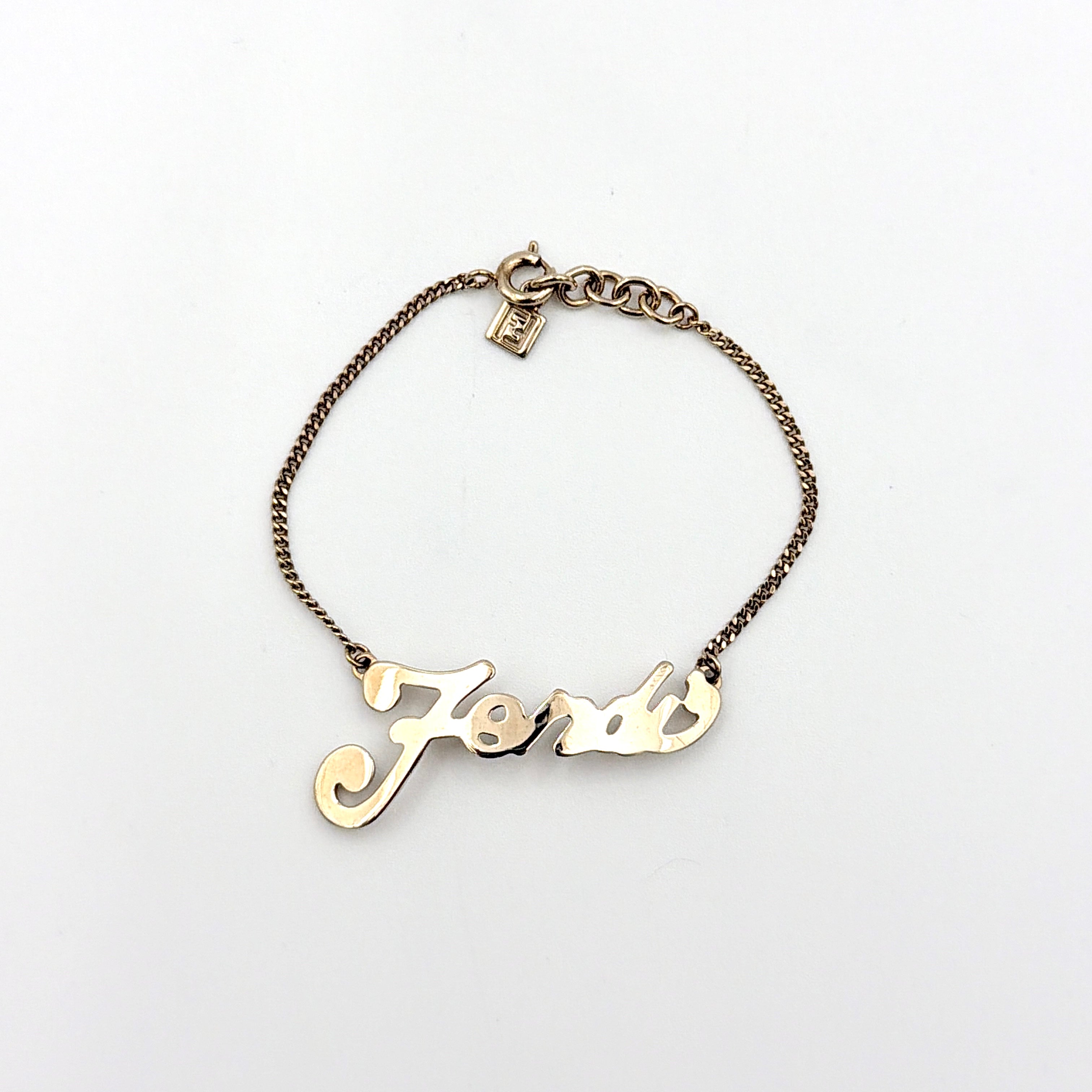 A gold-tone Fendi bracelet with a flowing logo script and adjustable chain, styled with a branded charm.