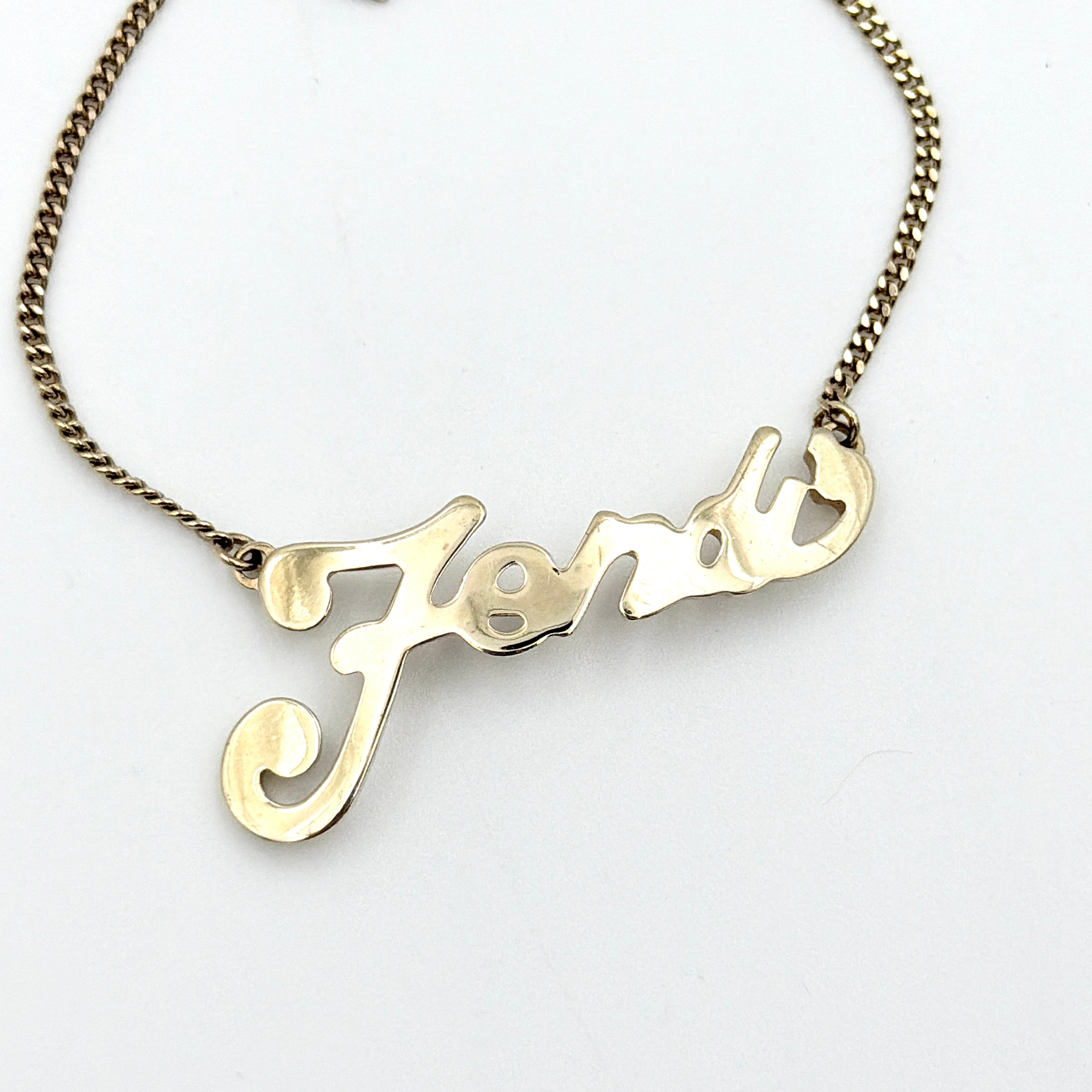 A gold-tone Fendi bracelet with a flowing logo script and adjustable chain, styled with a branded charm.