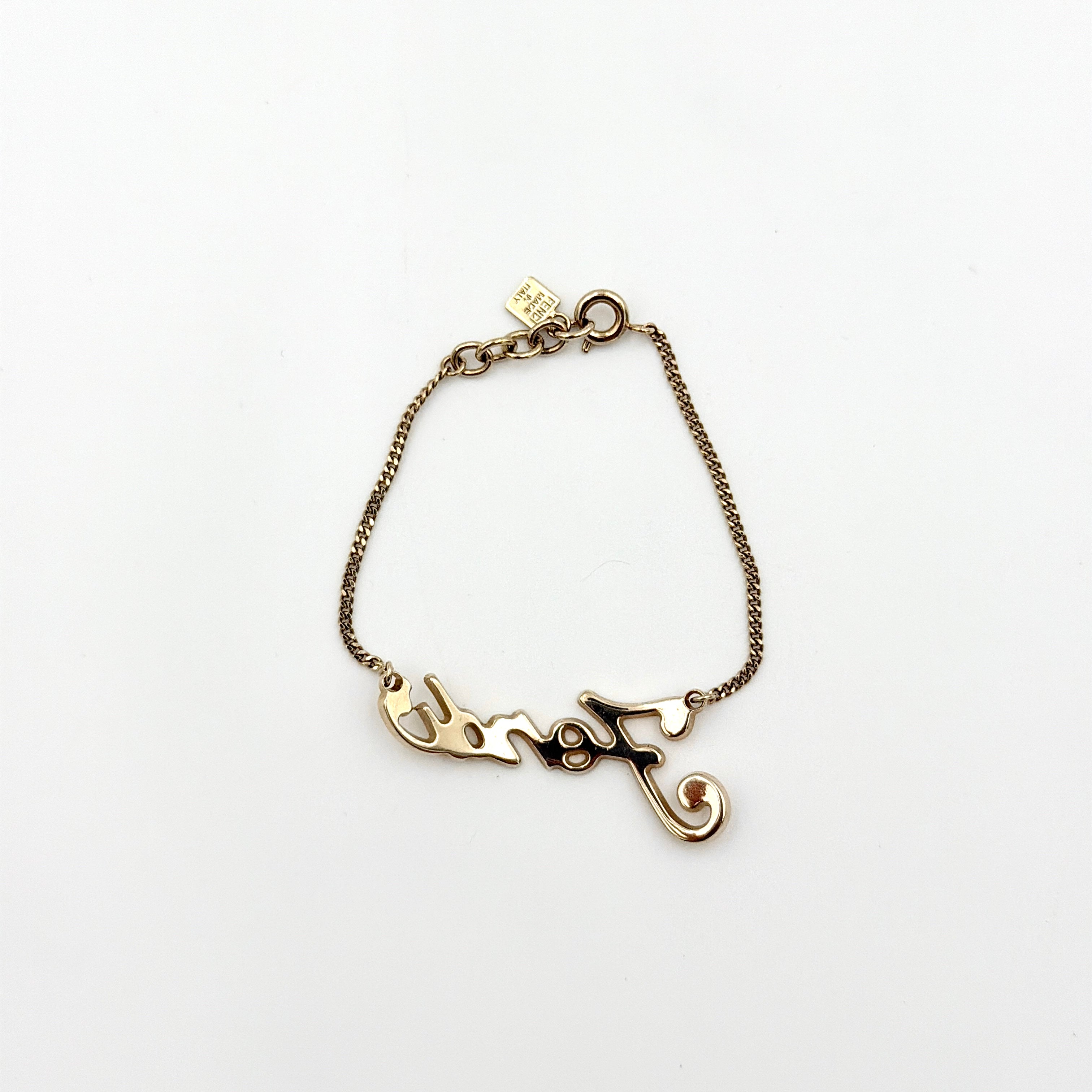 A gold-tone Fendi bracelet with a flowing logo script and adjustable chain, styled with a branded charm.