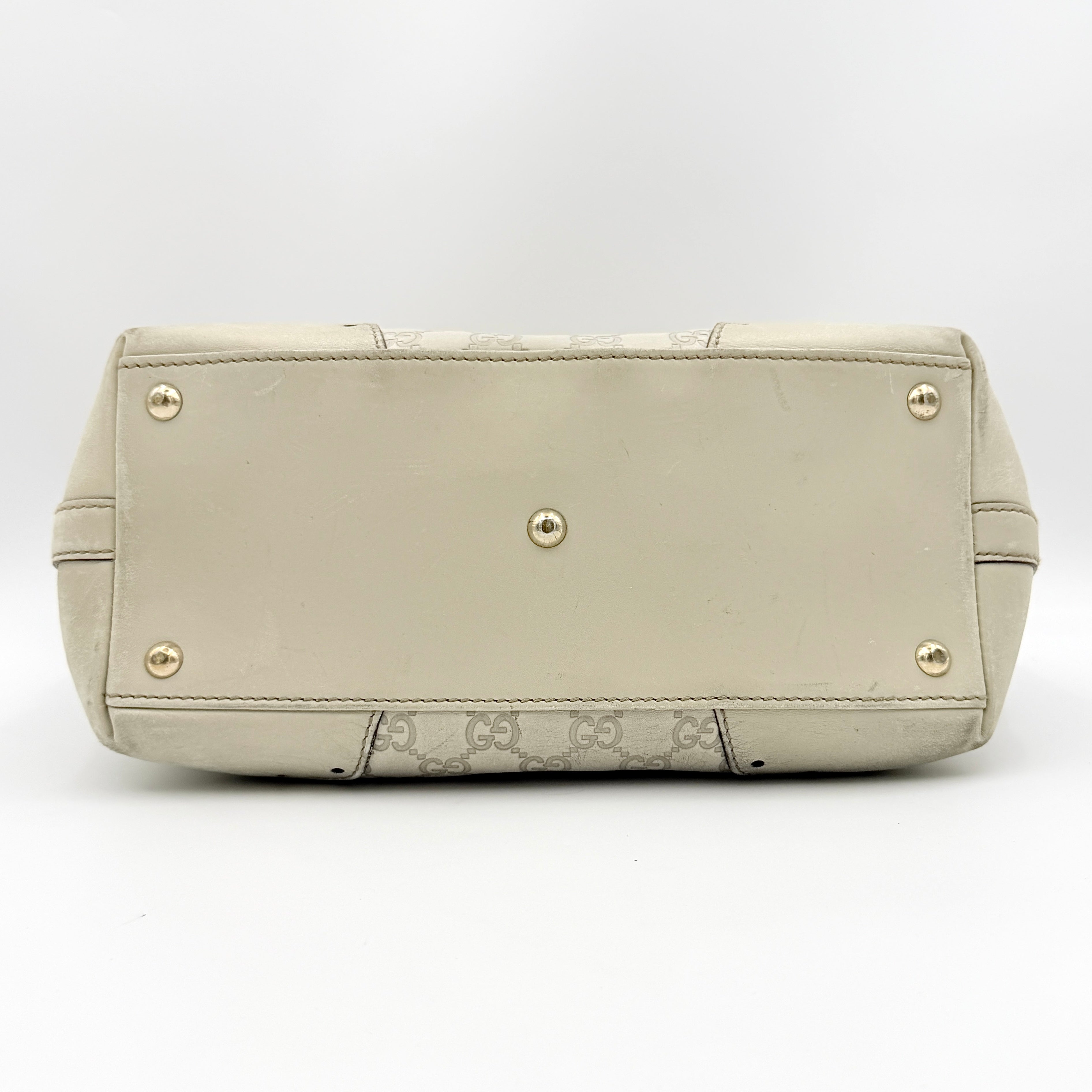 Cream Gucci GG Monogram Guccissima Punch Shoulder Bag with gold hardware, sculpted corners, and double top handles against a white background.
