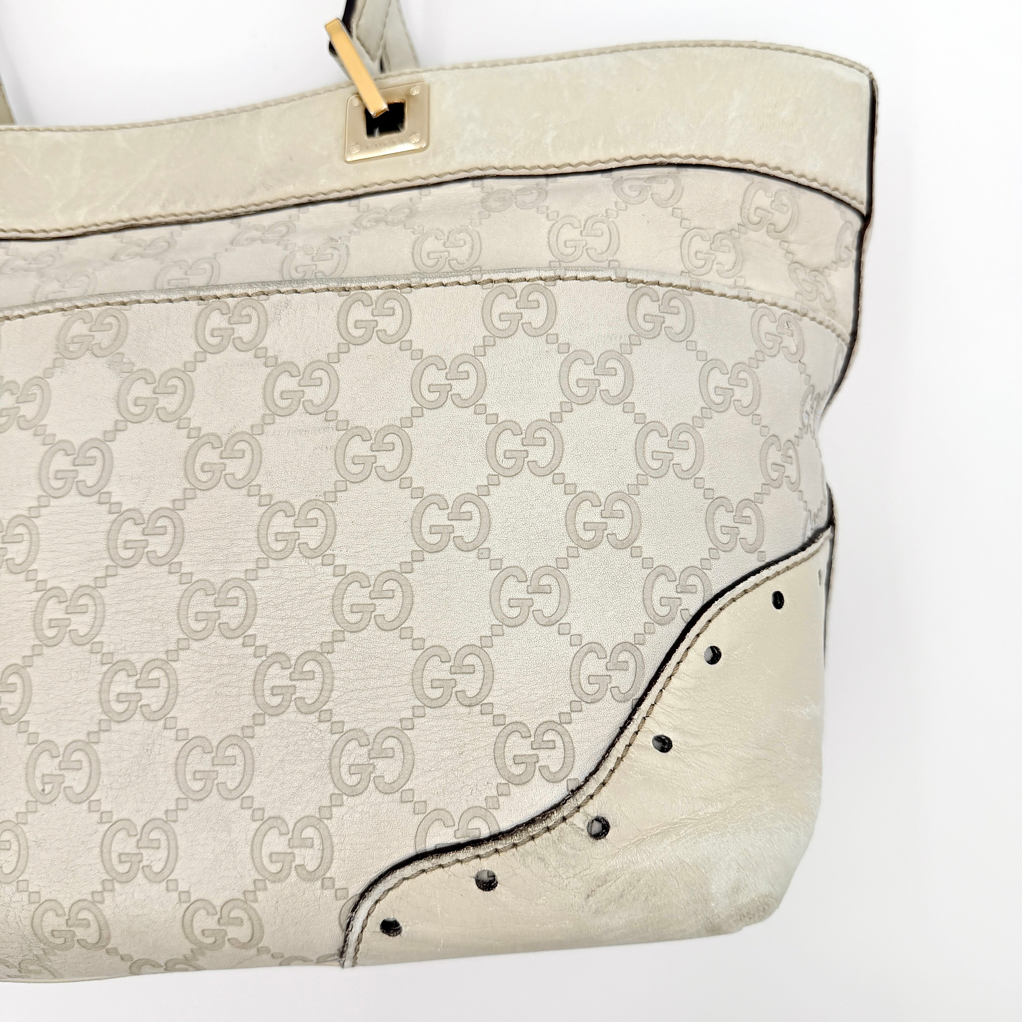 Cream Gucci GG Monogram Guccissima Punch Shoulder Bag with gold hardware, sculpted corners, and double top handles against a white background.