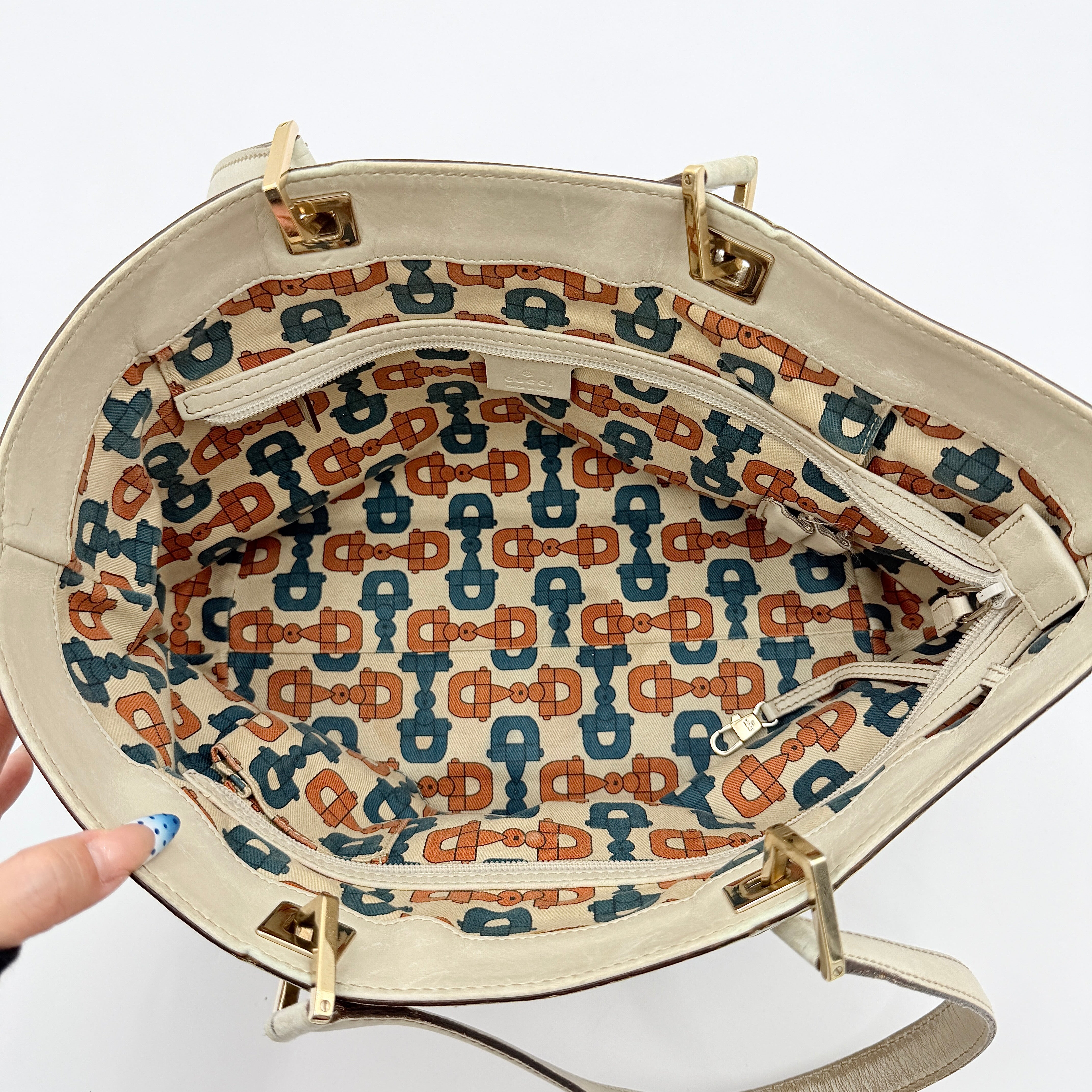 Cream Gucci GG Monogram Guccissima Punch Shoulder Bag with gold hardware, sculpted corners, and double top handles against a white background.