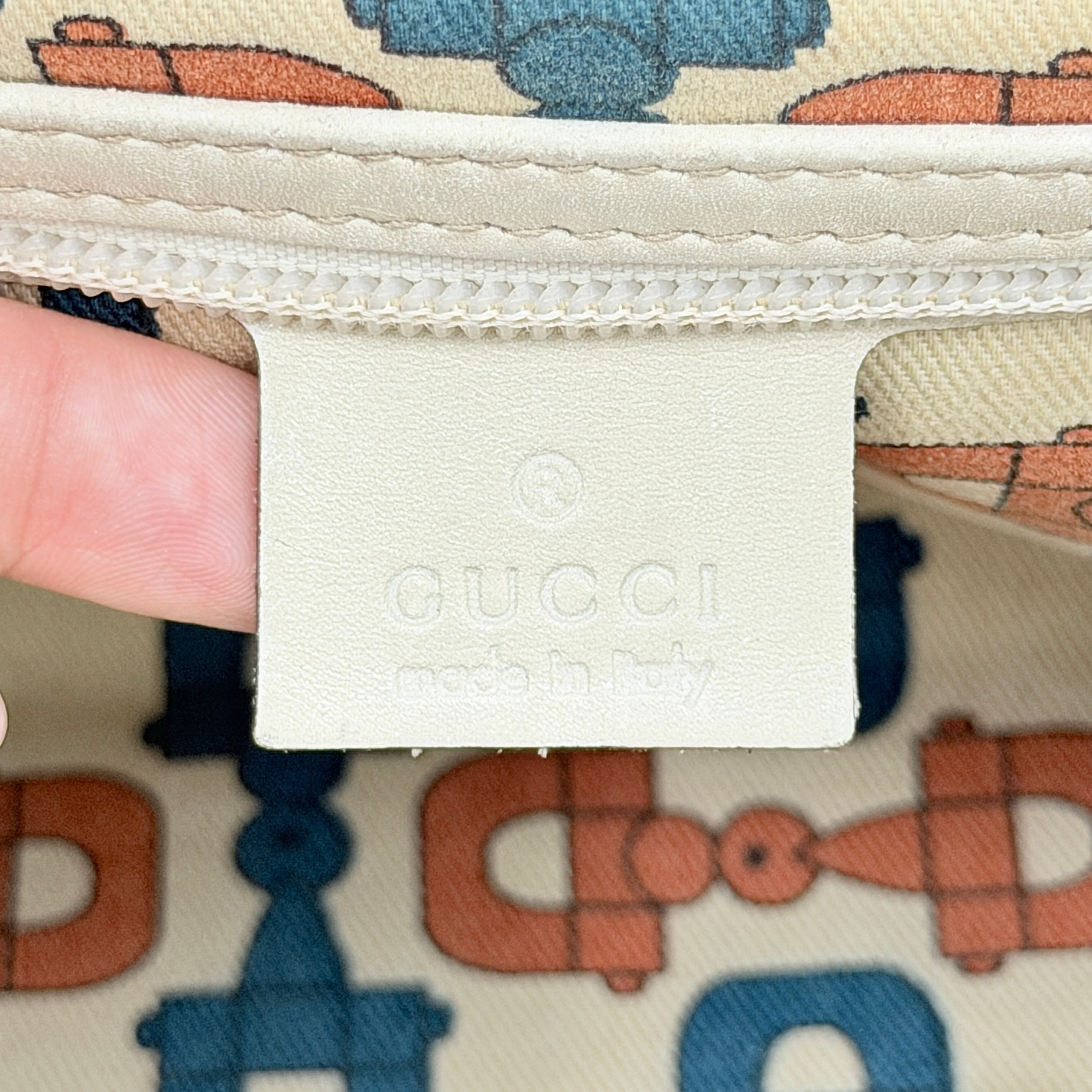 Cream Gucci GG Monogram Guccissima Punch Shoulder Bag with gold hardware, sculpted corners, and double top handles against a white background.