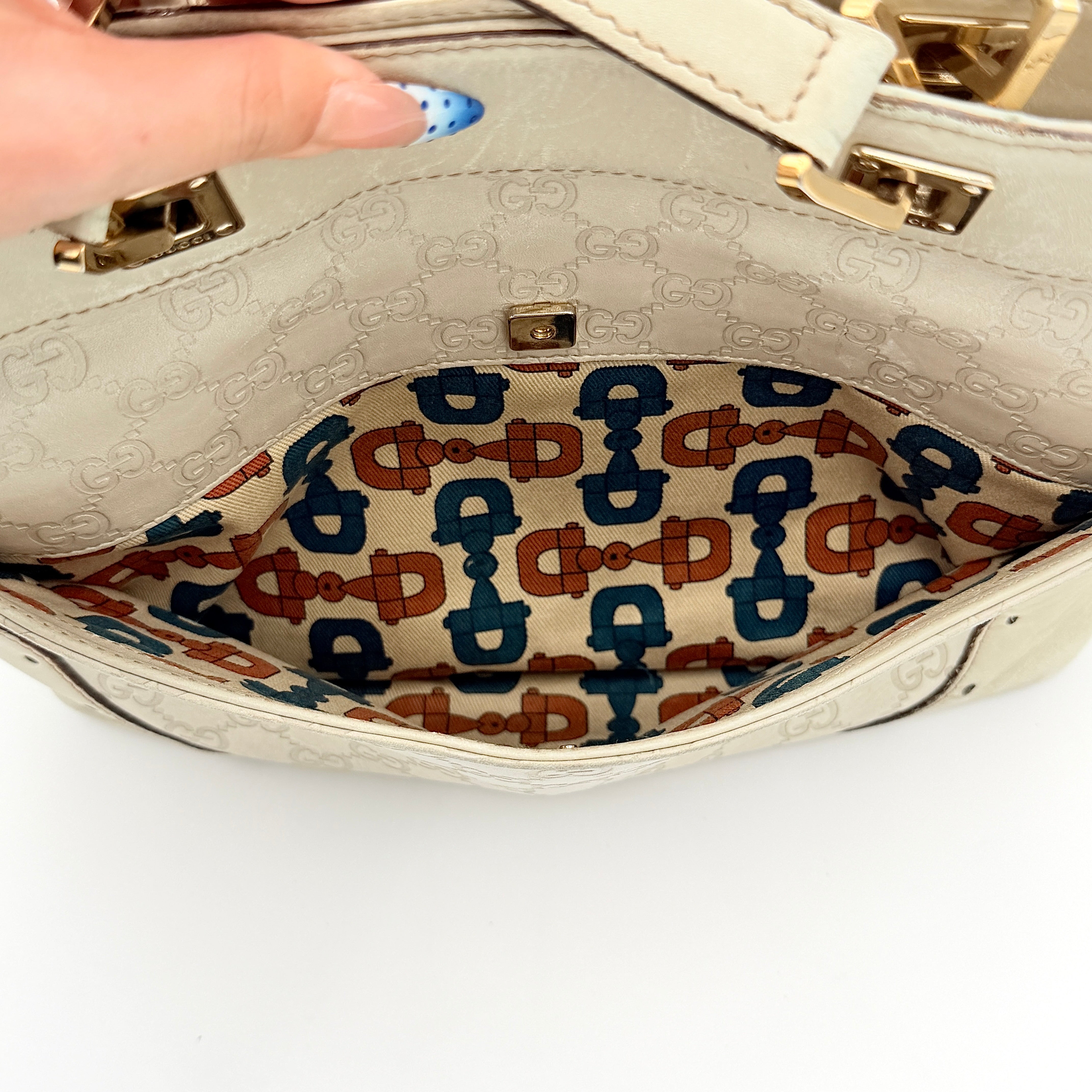 Cream Gucci GG Monogram Guccissima Punch Shoulder Bag with gold hardware, sculpted corners, and double top handles against a white background.