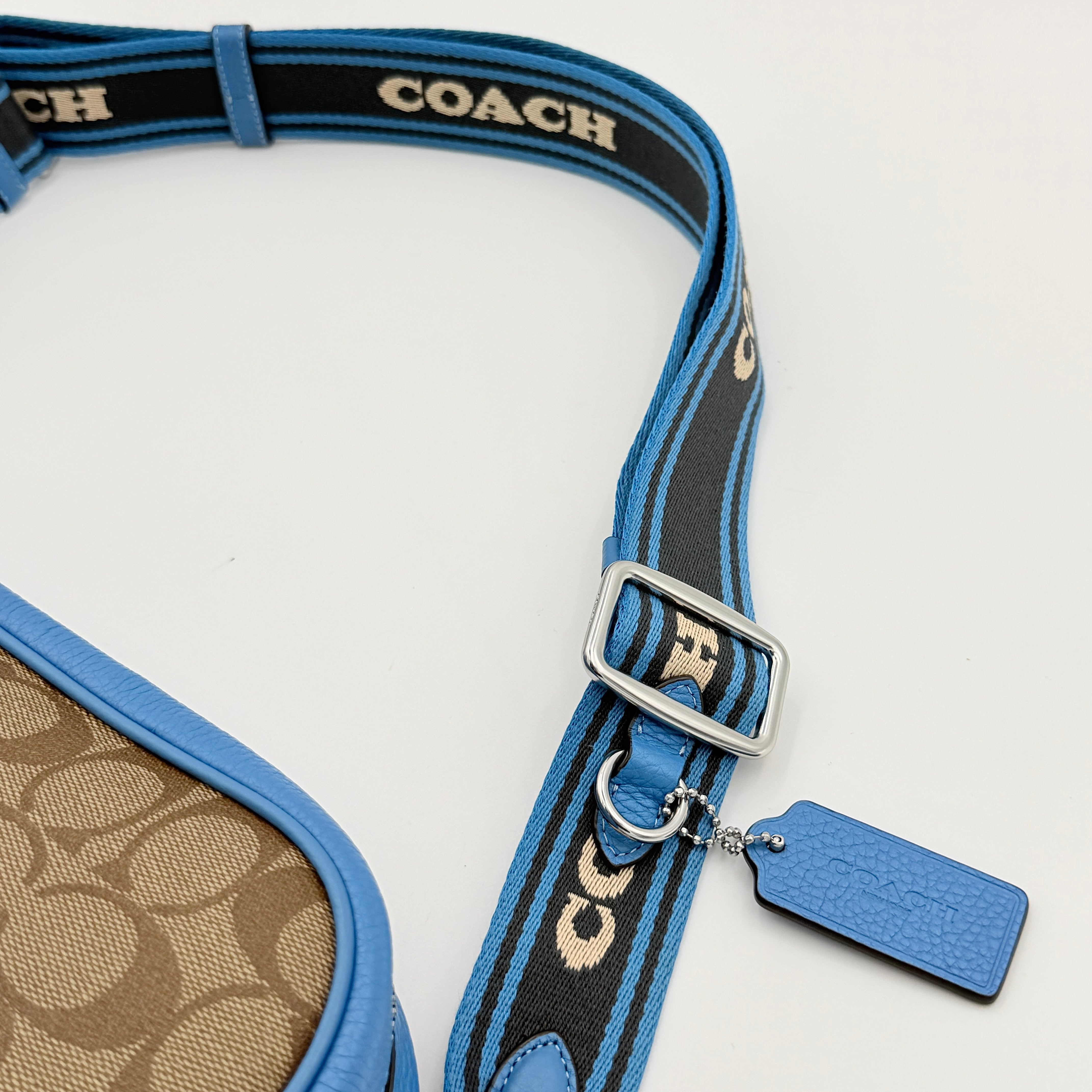 Coach Signature Jamie Crossbody Bag in beige and blue with bold logo webbing strap and blue leather trim, photographed against a white background.
