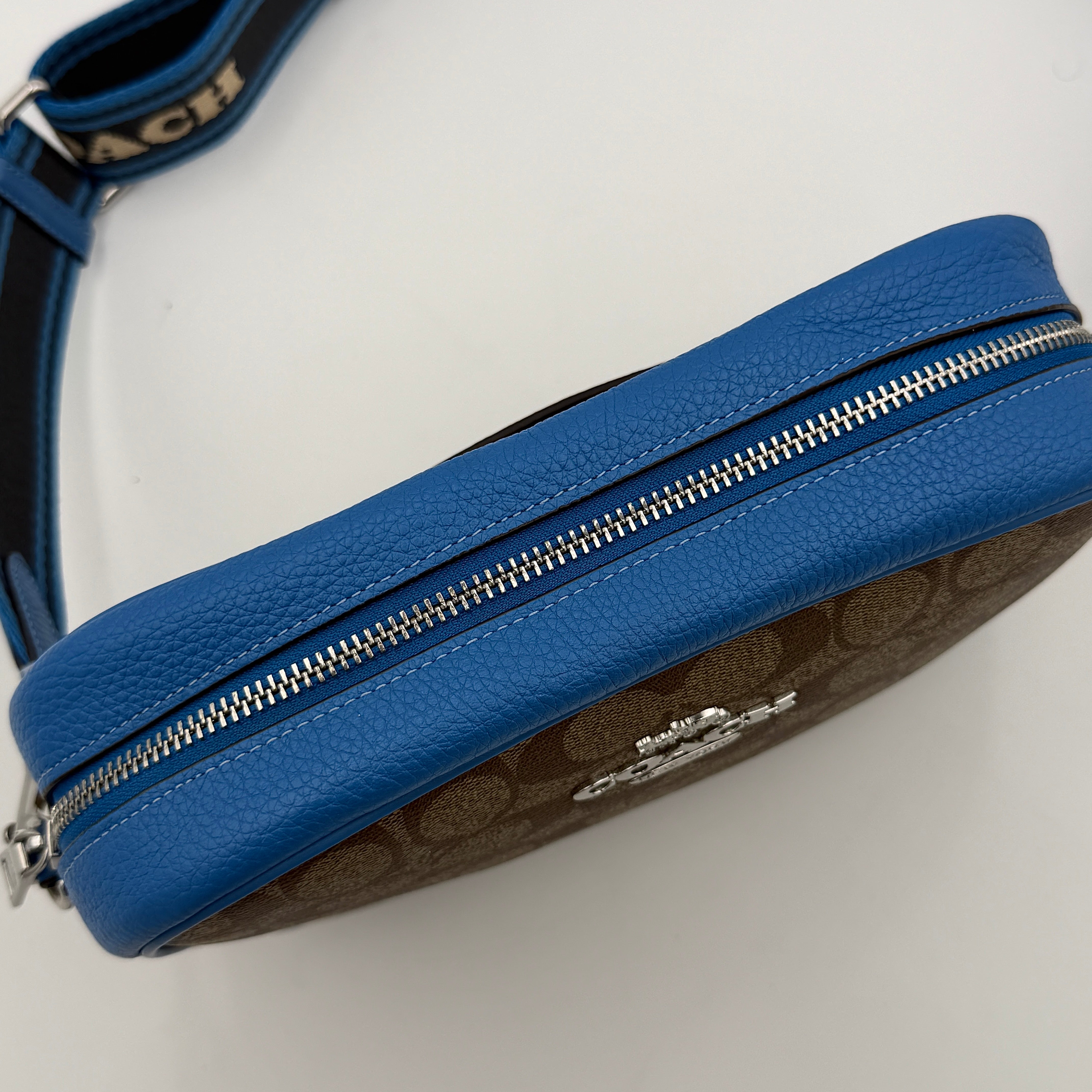 Coach Signature Jamie Crossbody Bag in beige and blue with bold logo webbing strap and blue leather trim, photographed against a white background.
