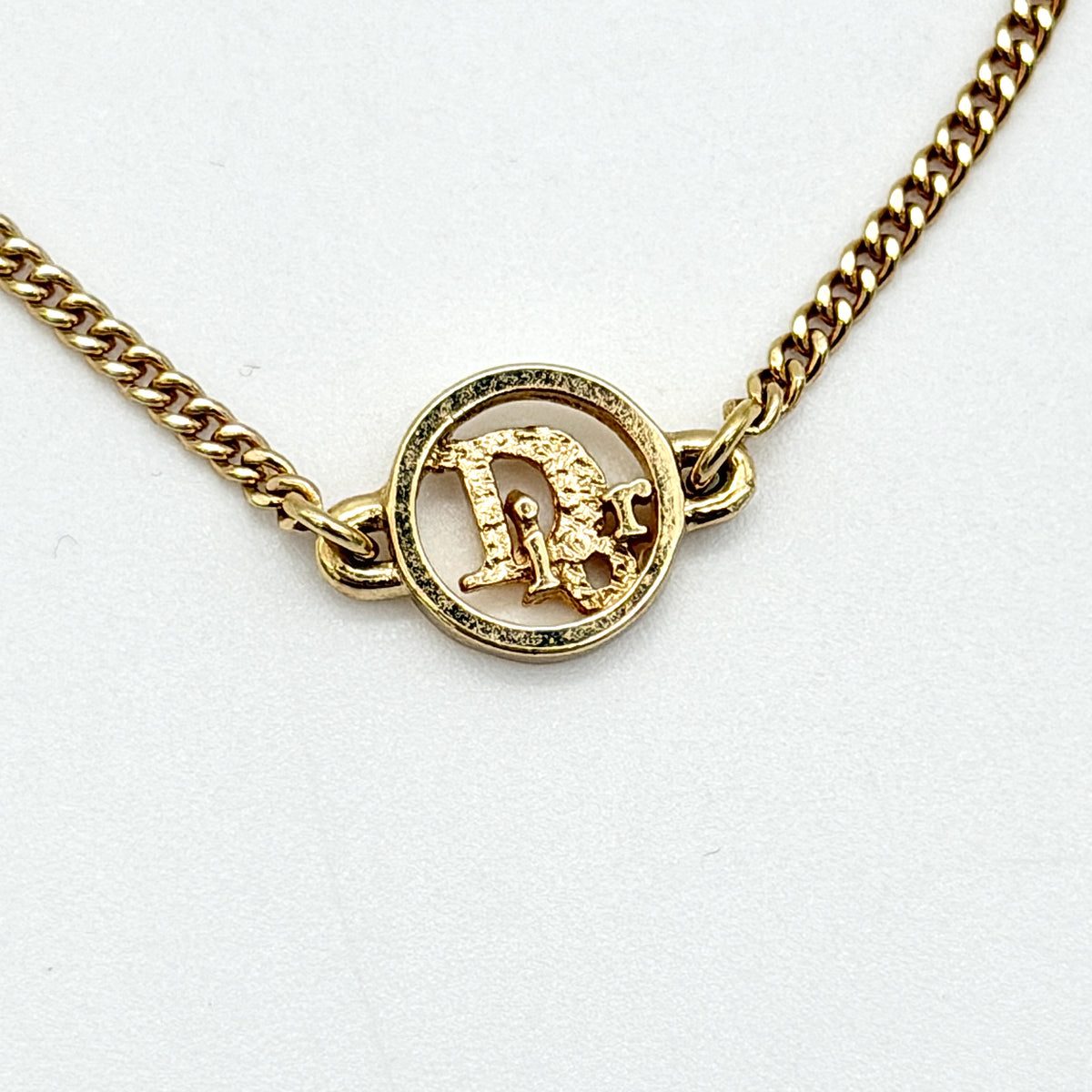 Dior gold-tone logo circle bracelet featuring a curb chain and textured central Dior emblem, photographed on a white background.