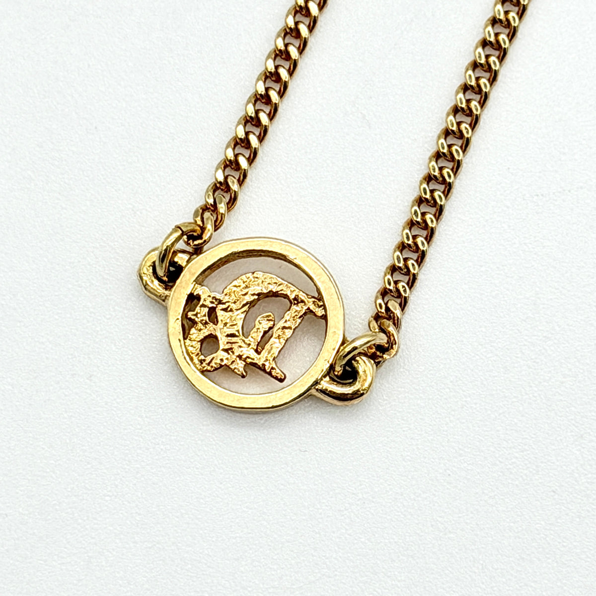 Dior gold-tone logo circle bracelet featuring a curb chain and textured central Dior emblem, photographed on a white background.