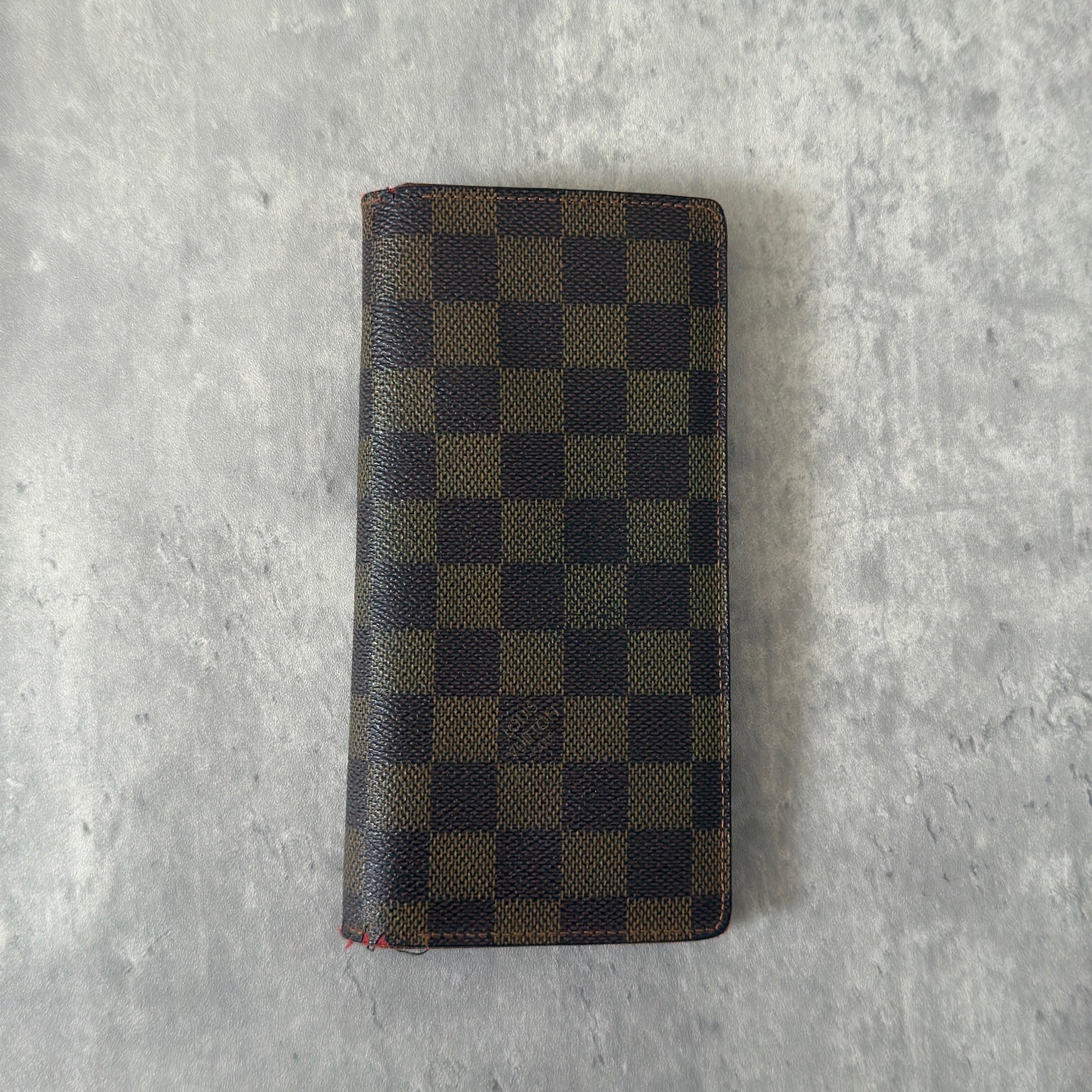 Louis Vuitton Damier Ebene Brazza wallet in dark brown and black checkered canvas, featuring a snap closure and organized interior with card slots and bill compartments.