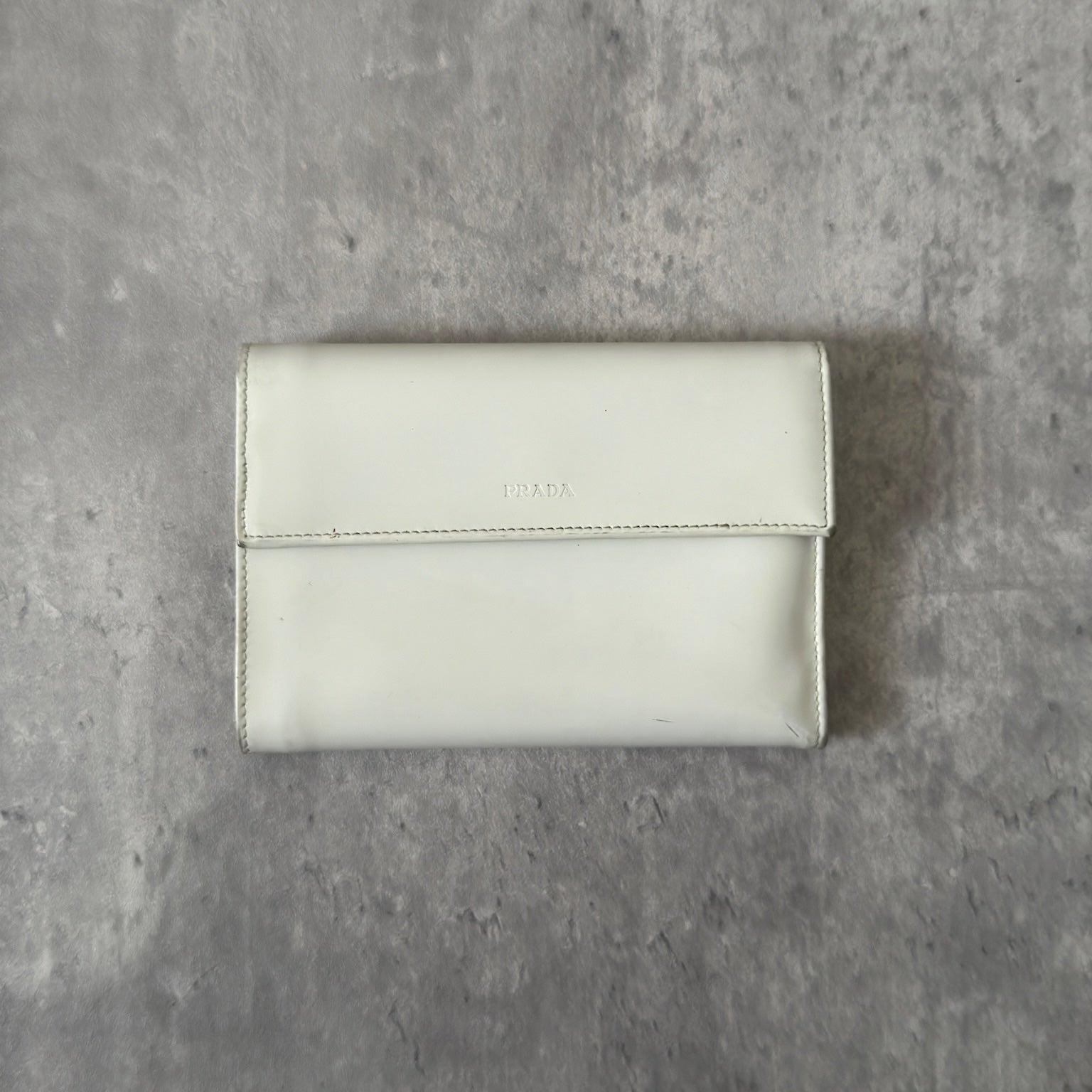 Prada City Calf Leather Compact Wallet in off-white with flap closure and embossed logo detail, showcasing a sophisticated, minimalist design.