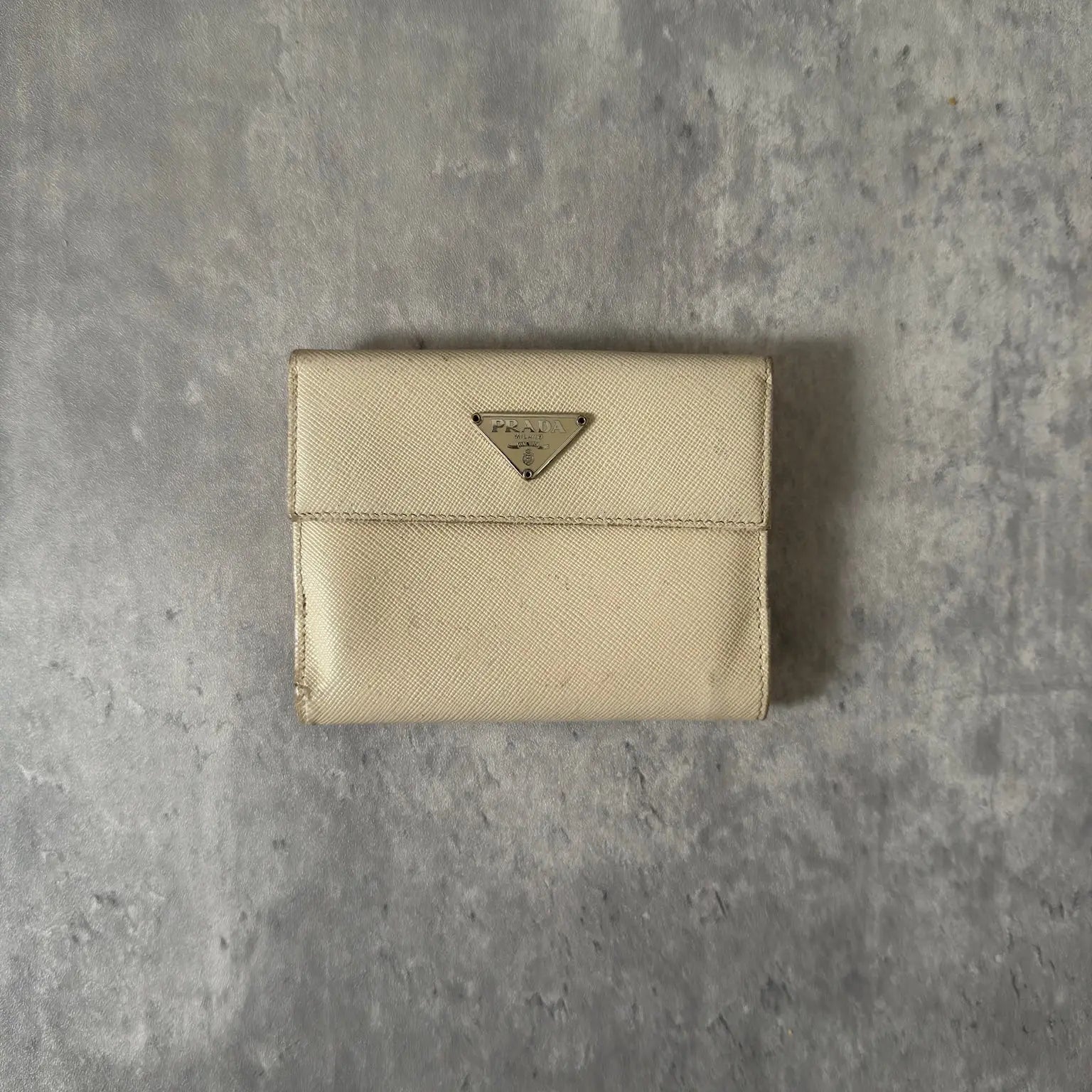 Prada Cream Saffiano Folding Leather Wallet, crafted from textured Saffiano leather with a gold-tone triangular logo and a compact folding design.