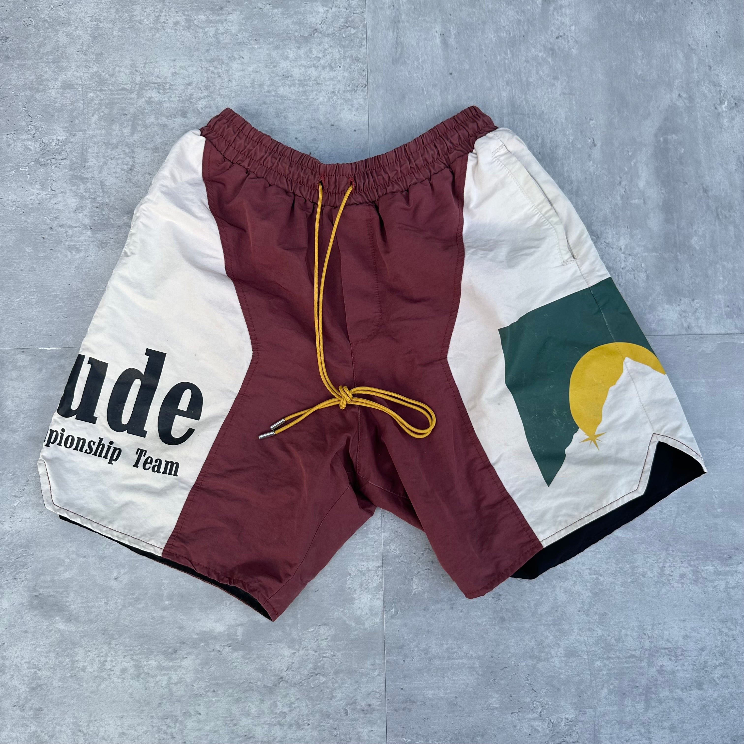 Rhude Panel Logo Shorts Maroon/White/Multi FW22, featuring championship print and moon graphic, with yellow drawstring and bold panel design.