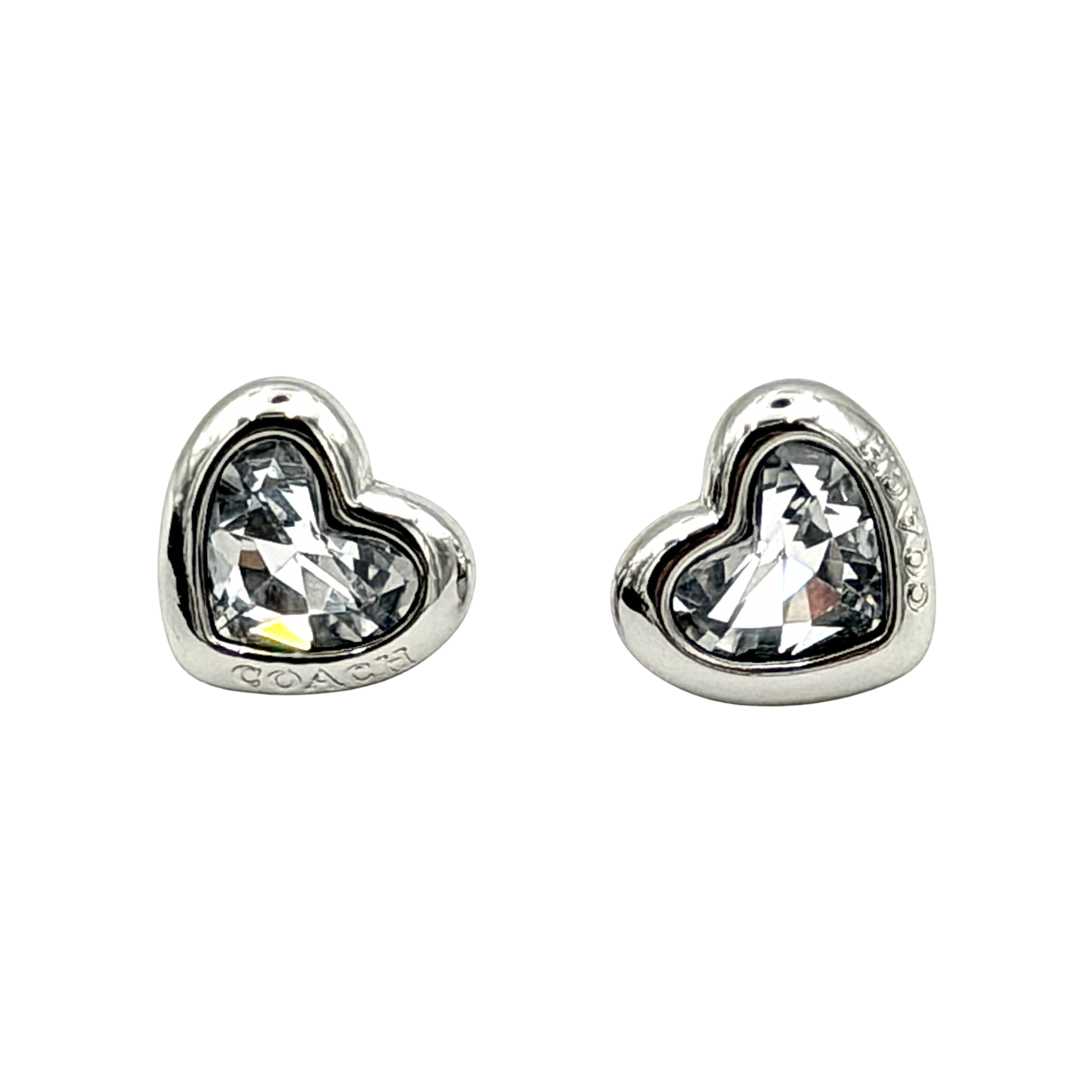 A pair of Coach heart-shaped crystal stud earrings in silver-tone metal with engraved logo and faceted stones.