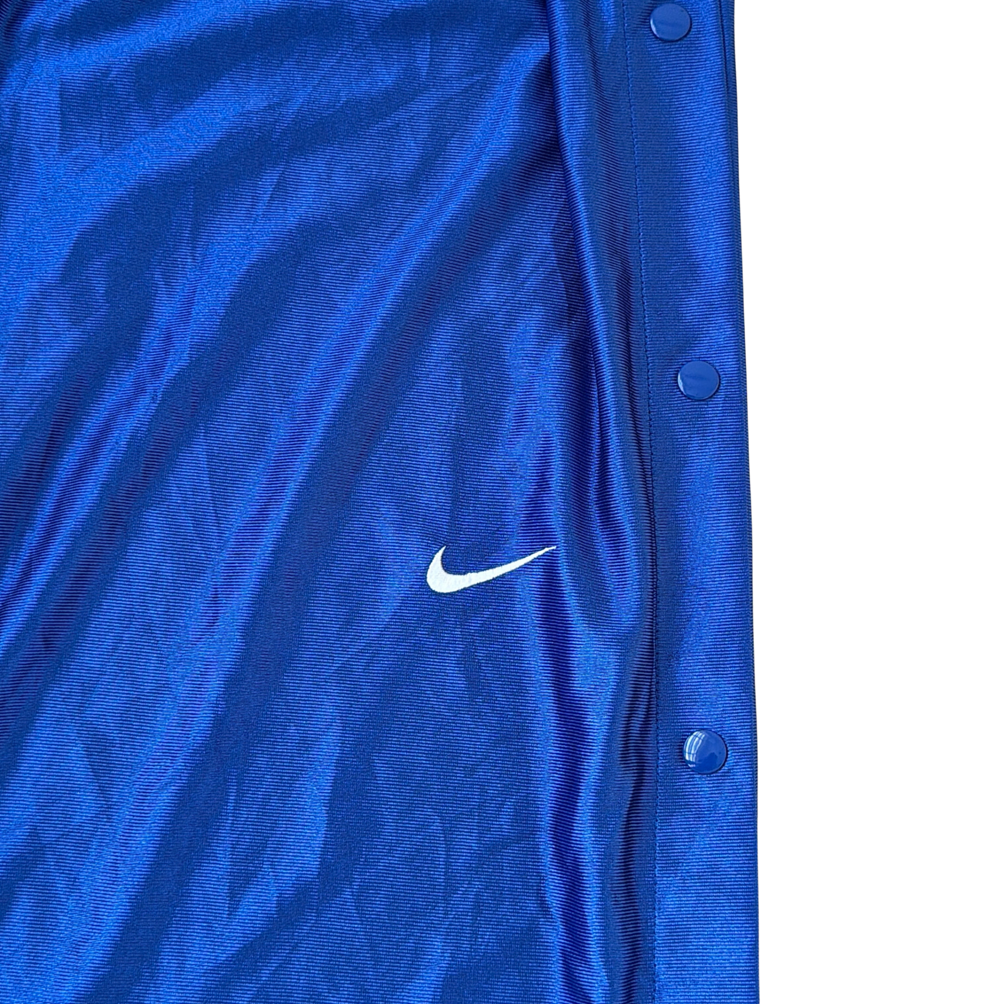 Electric blue Nike tear away track pants with snap button sides and white Swoosh logo displayed flat against a black background.