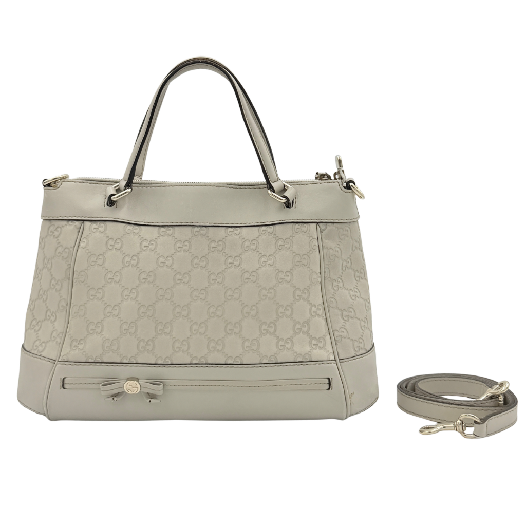 Gucci Mayfair Bow 2Way shoulder bag in cream GG monogram leather with dual handles and detachable strap, styled against a neutral backdrop.