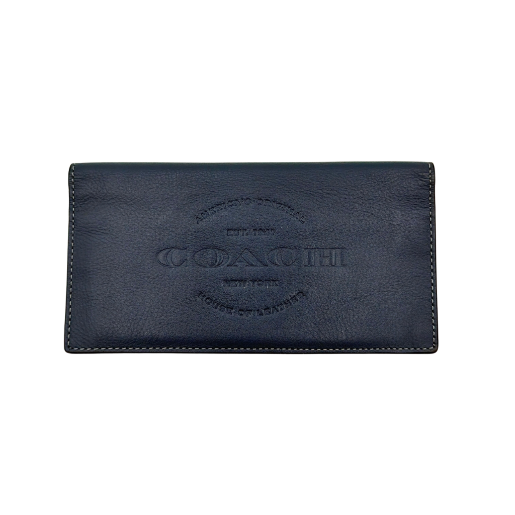 Coach Flap Long Wallet in navy blue leather with embossed logo, shown in a crisp editorial front view.