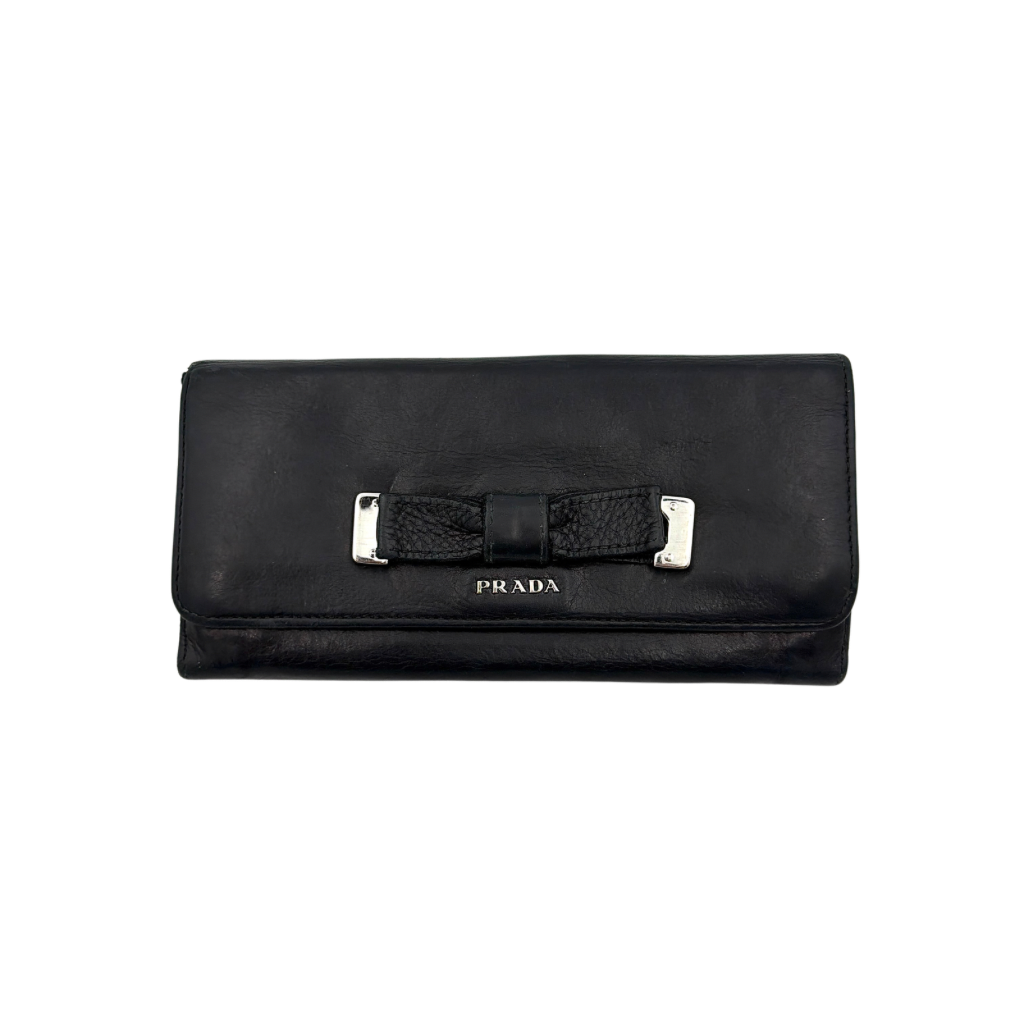 Prada Fiocco Bow Continental Wallet in black leather with a central grosgrain bow and silver-tone accents, displayed with refined simplicity.