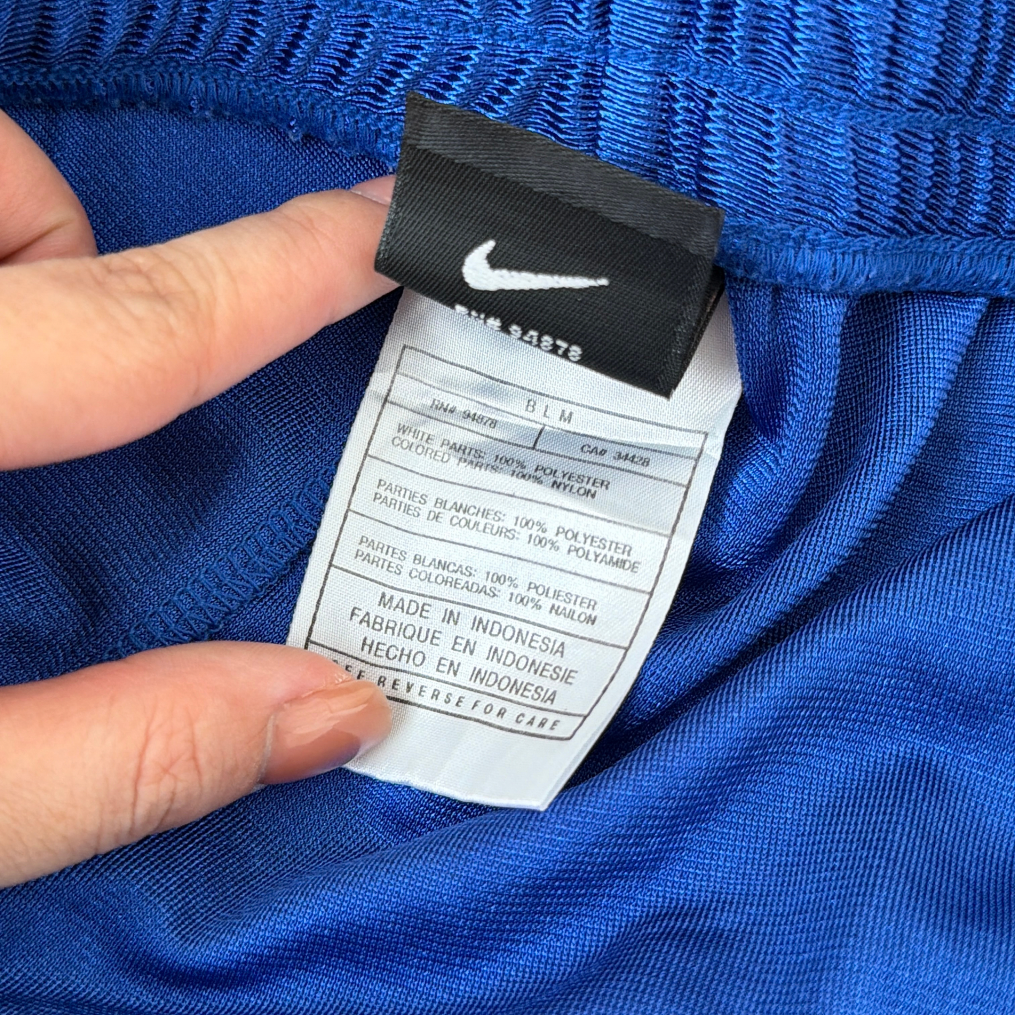 Electric blue Nike tear away track pants with snap button sides and white Swoosh logo displayed flat against a black background.