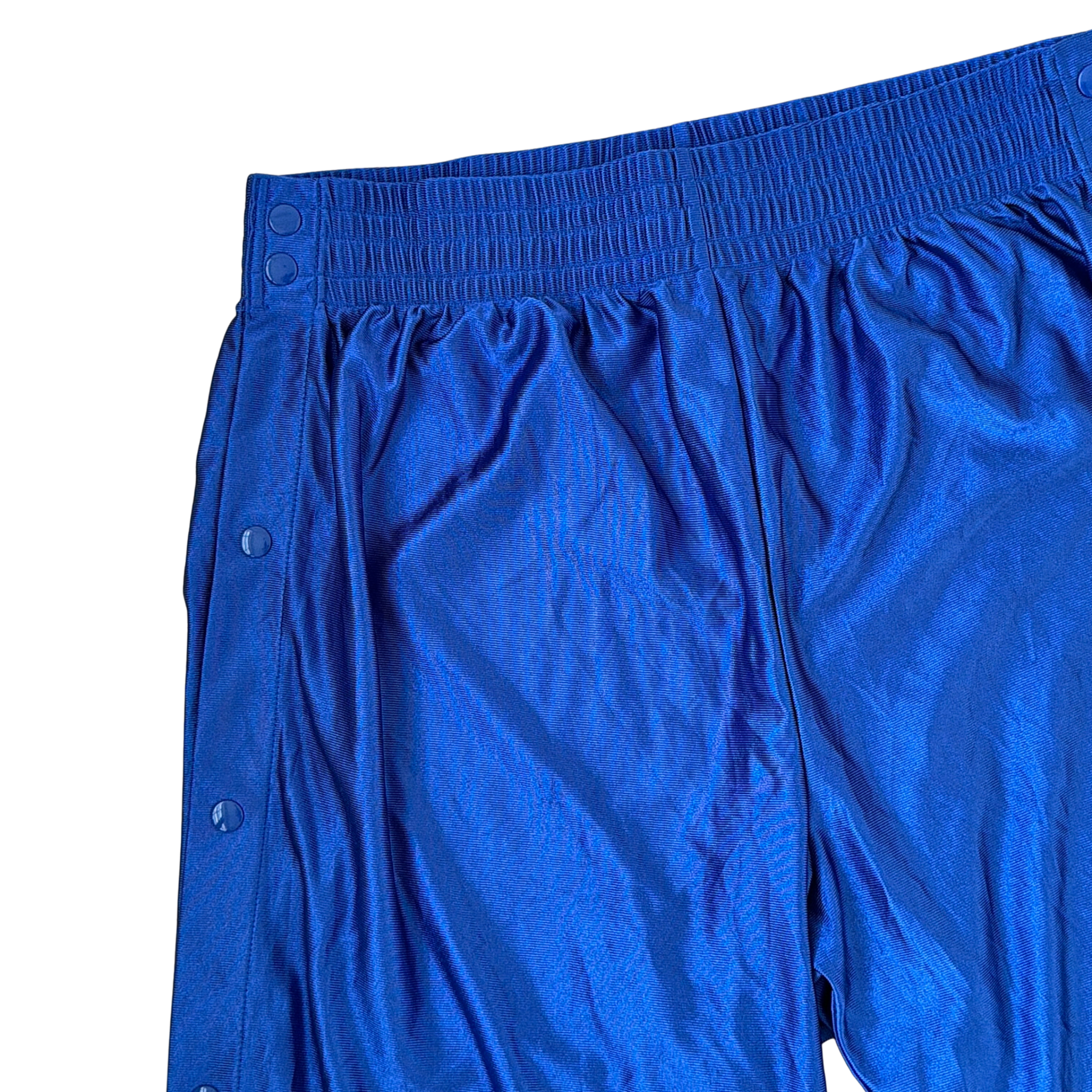 Electric blue Nike tear away track pants with snap button sides and white Swoosh logo displayed flat against a black background.