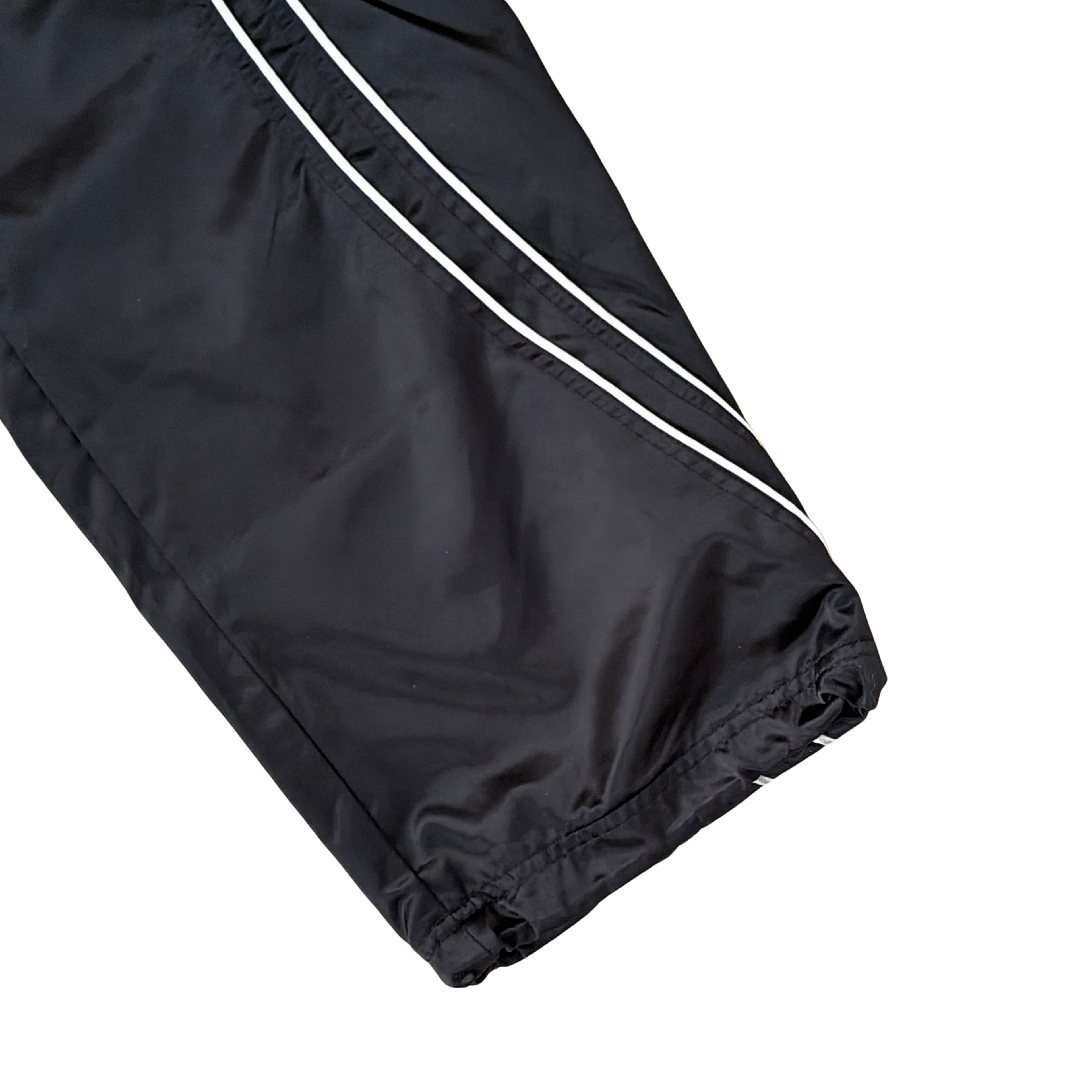 Supreme black satin track pants with white piping, a crest and Supreme logo embroidery at the hip, styled with relaxed legs.